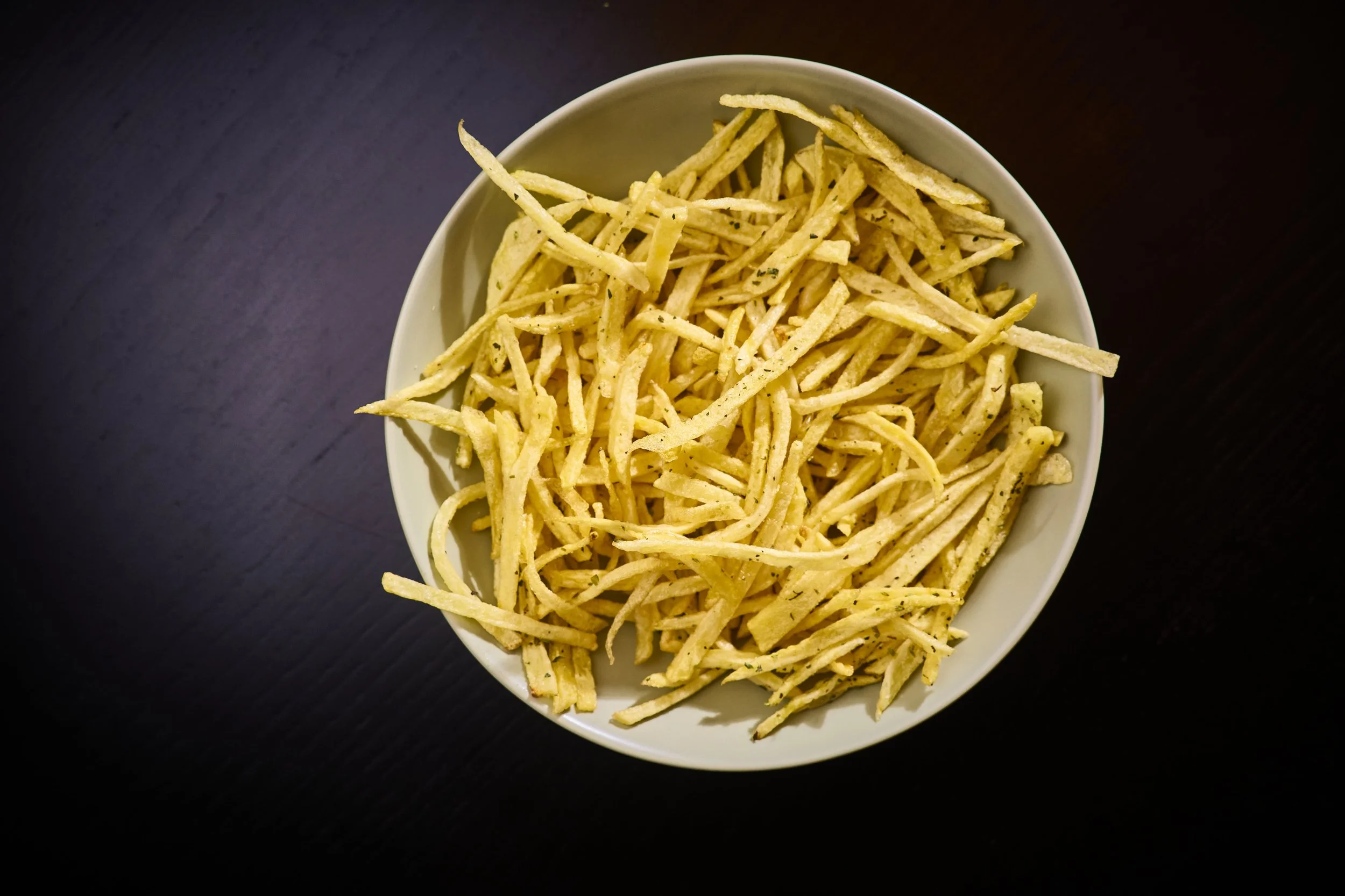 Porção de palitos de farinha de milho, empilhados em uma tigela branca sobre uma mesa escura.