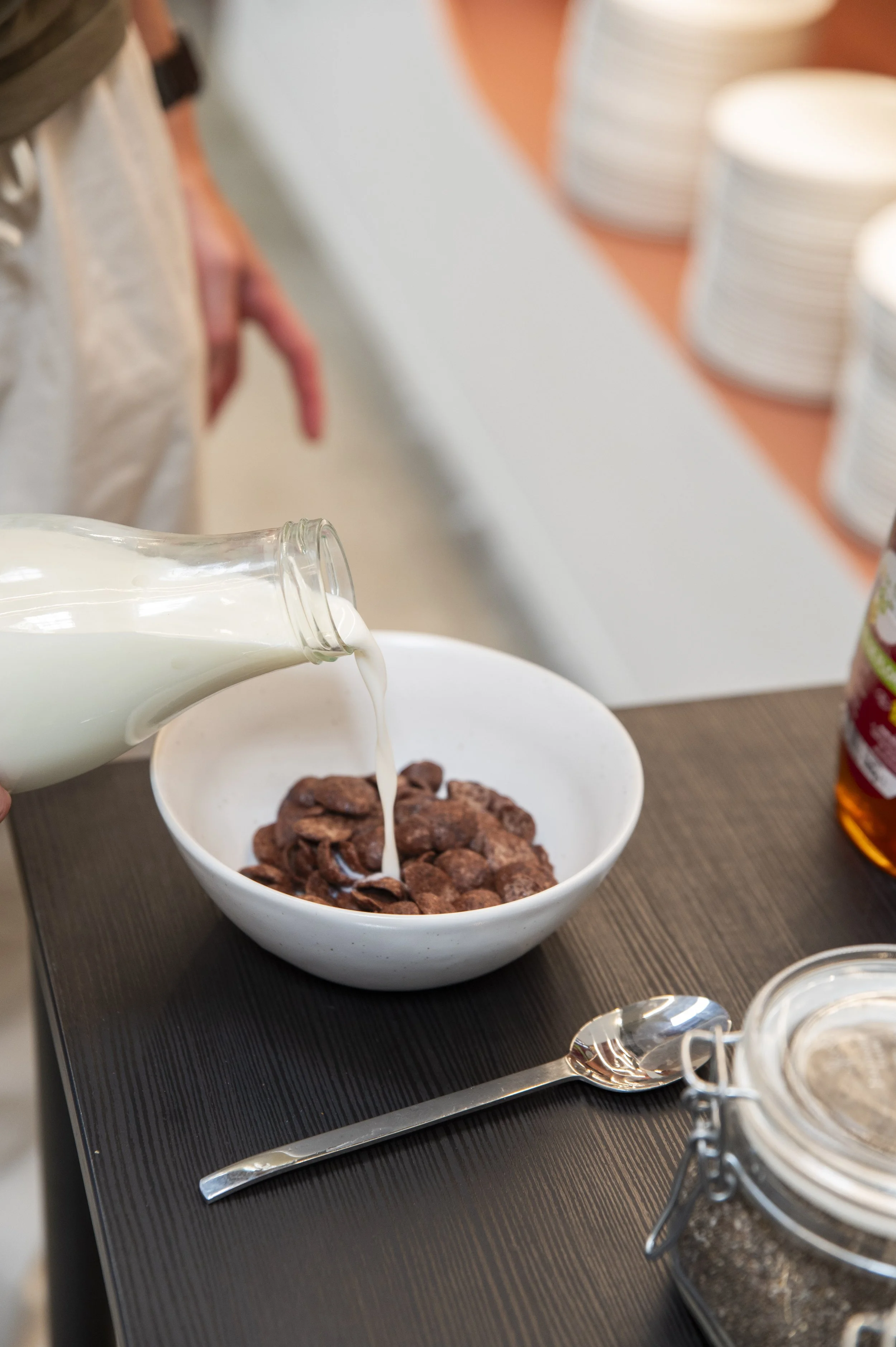 Pessoa despejando leite sobre uma tigela de cereais de chocolate.