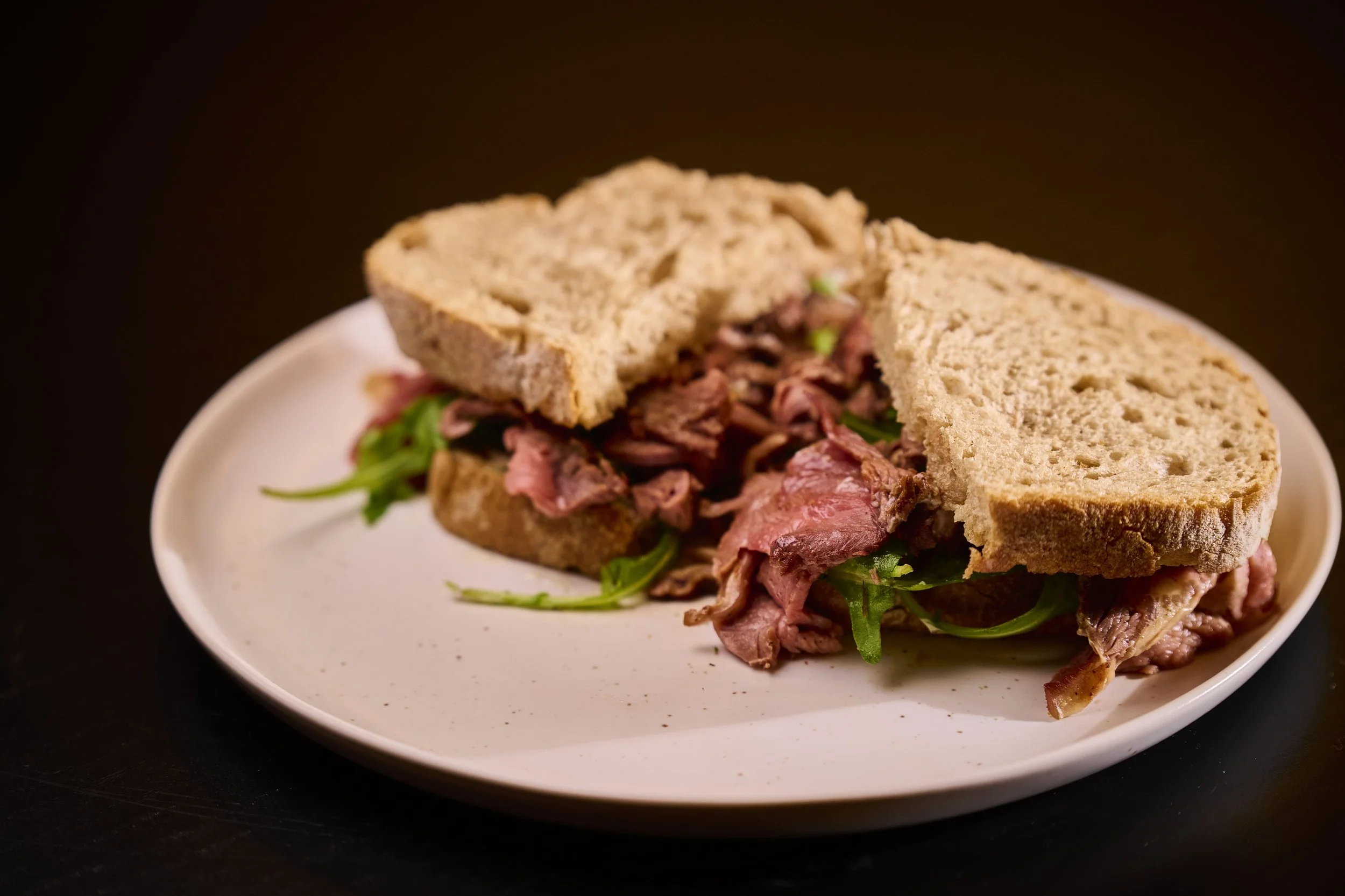 Sanduíche de carne assada com pão integral e folhas verdes em um prato branco