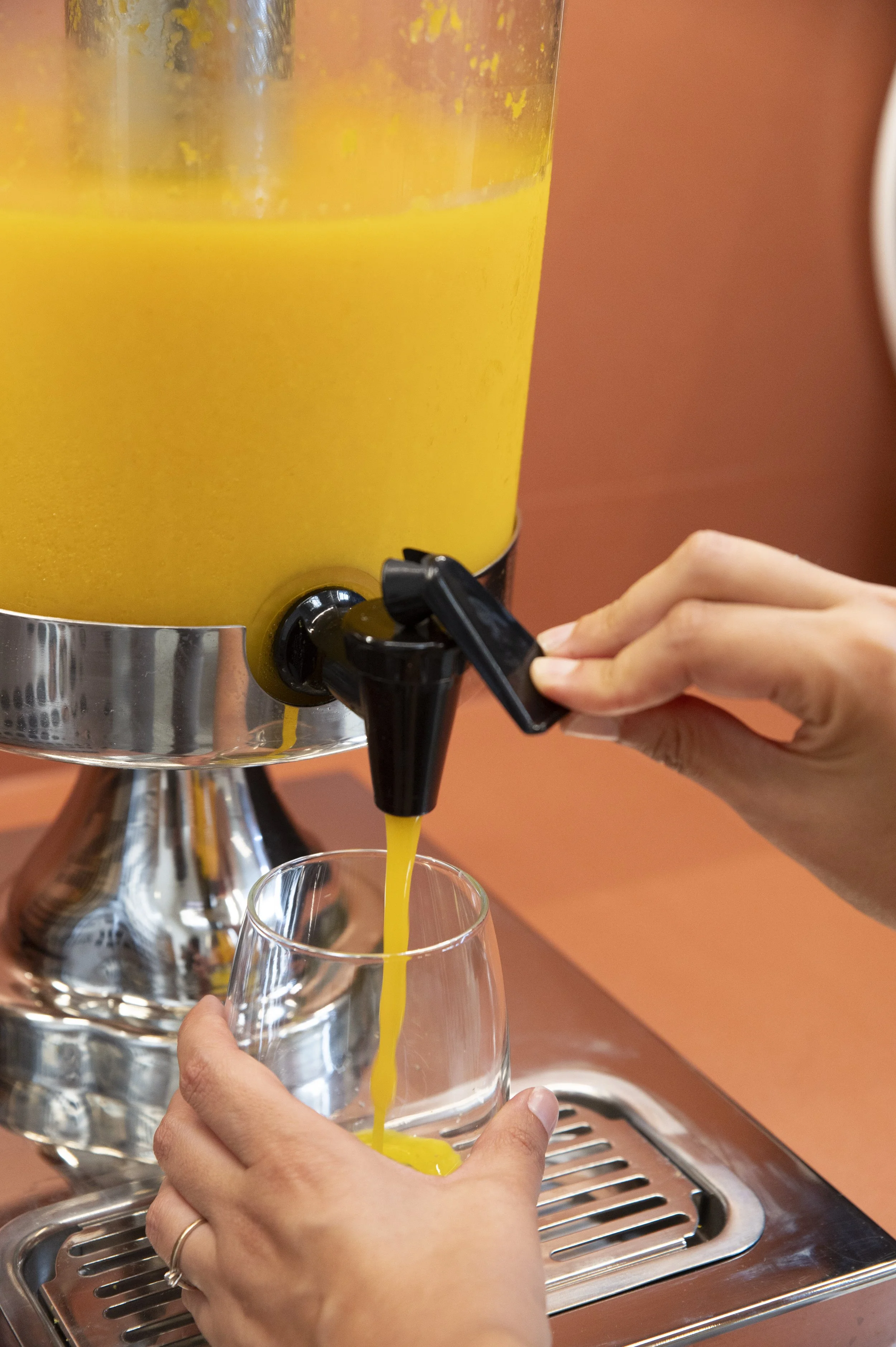 Pessoas servindo suco de laranja de uma jarra através de uma torneira em um copo de vidro.