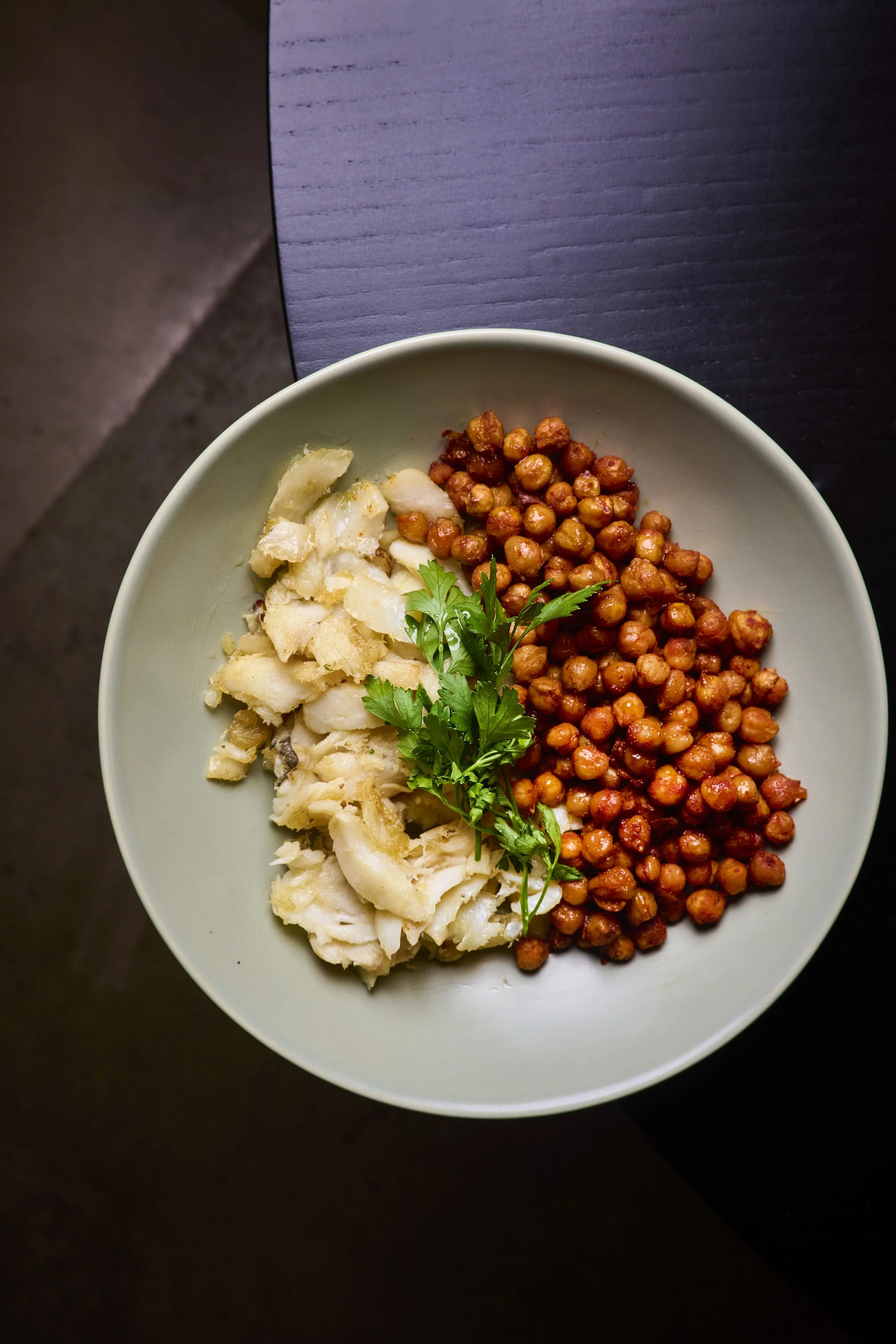 Prato com peixe, grão de bico temperado e uma folha de salsa