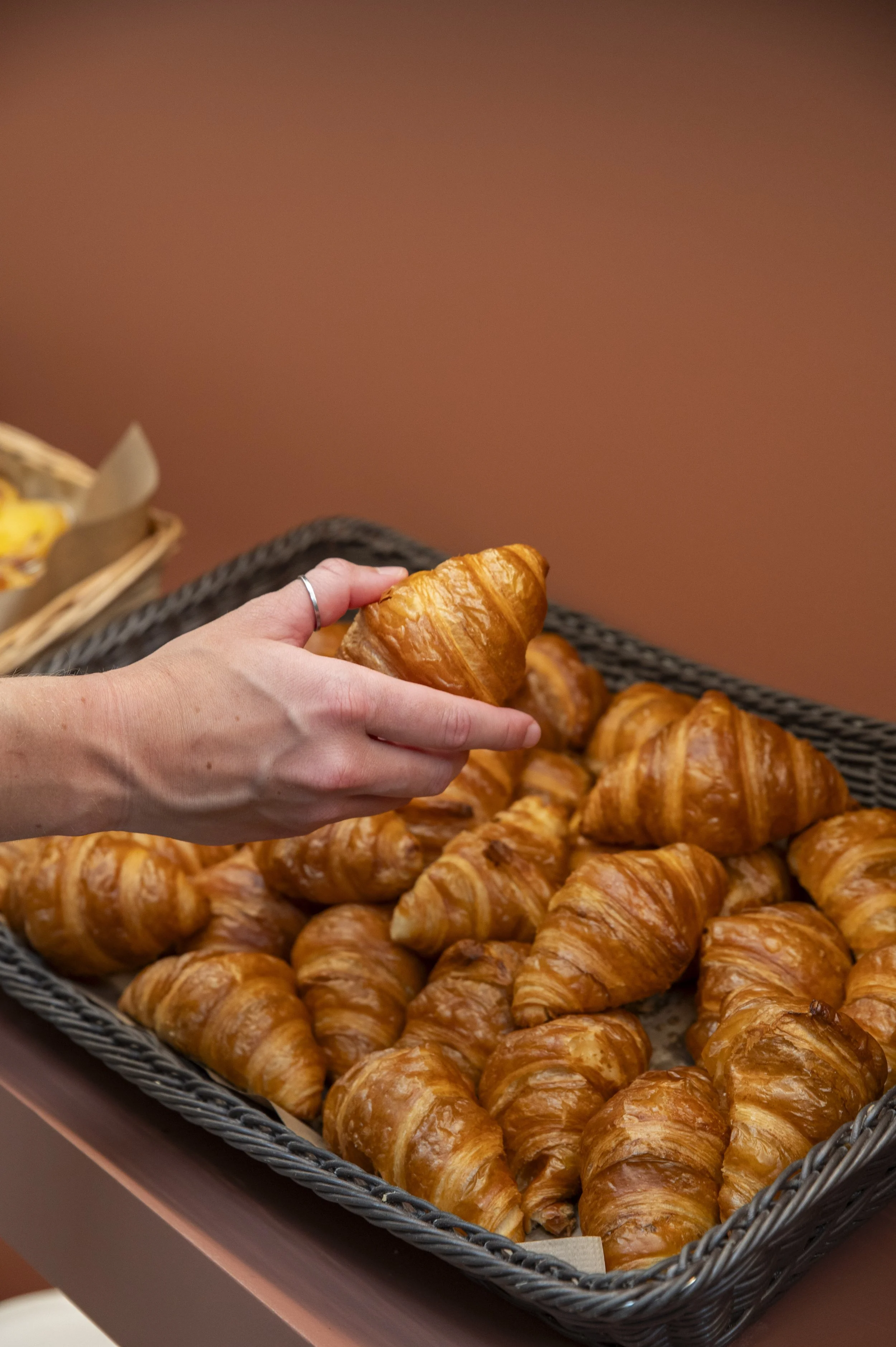 Pessoa pegando um croissant em uma cesta cheia de croissants frescos.