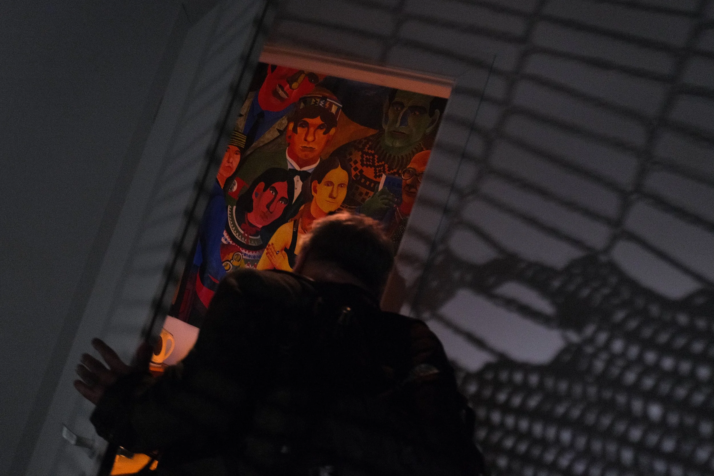 In the foreground, a man is opening a door to a room. As the door opens, we see faces from a painting on the wall, staring at the man.