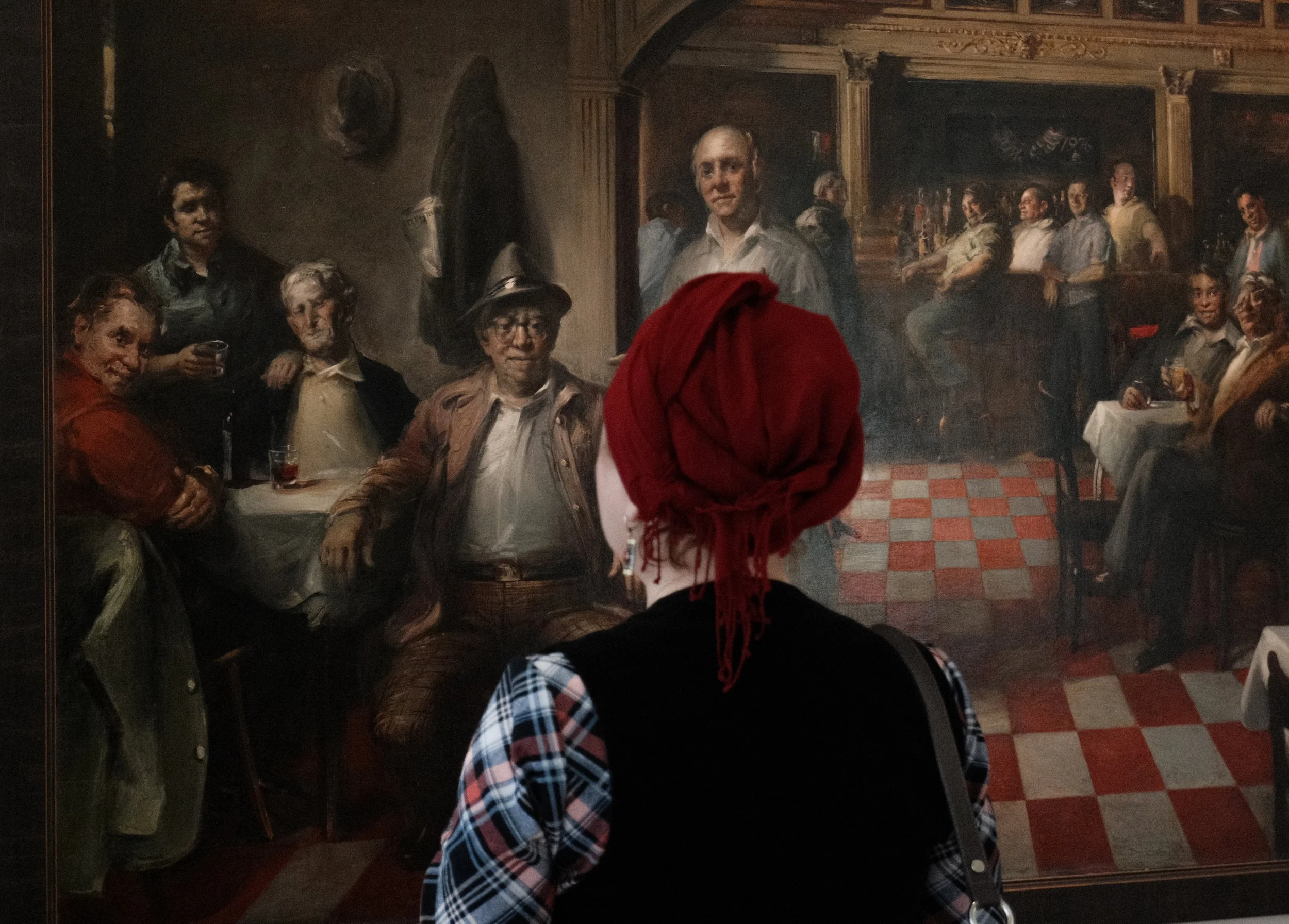 A woman with a maroon headband and plaid shirt observing a mural of people in a bar setting.