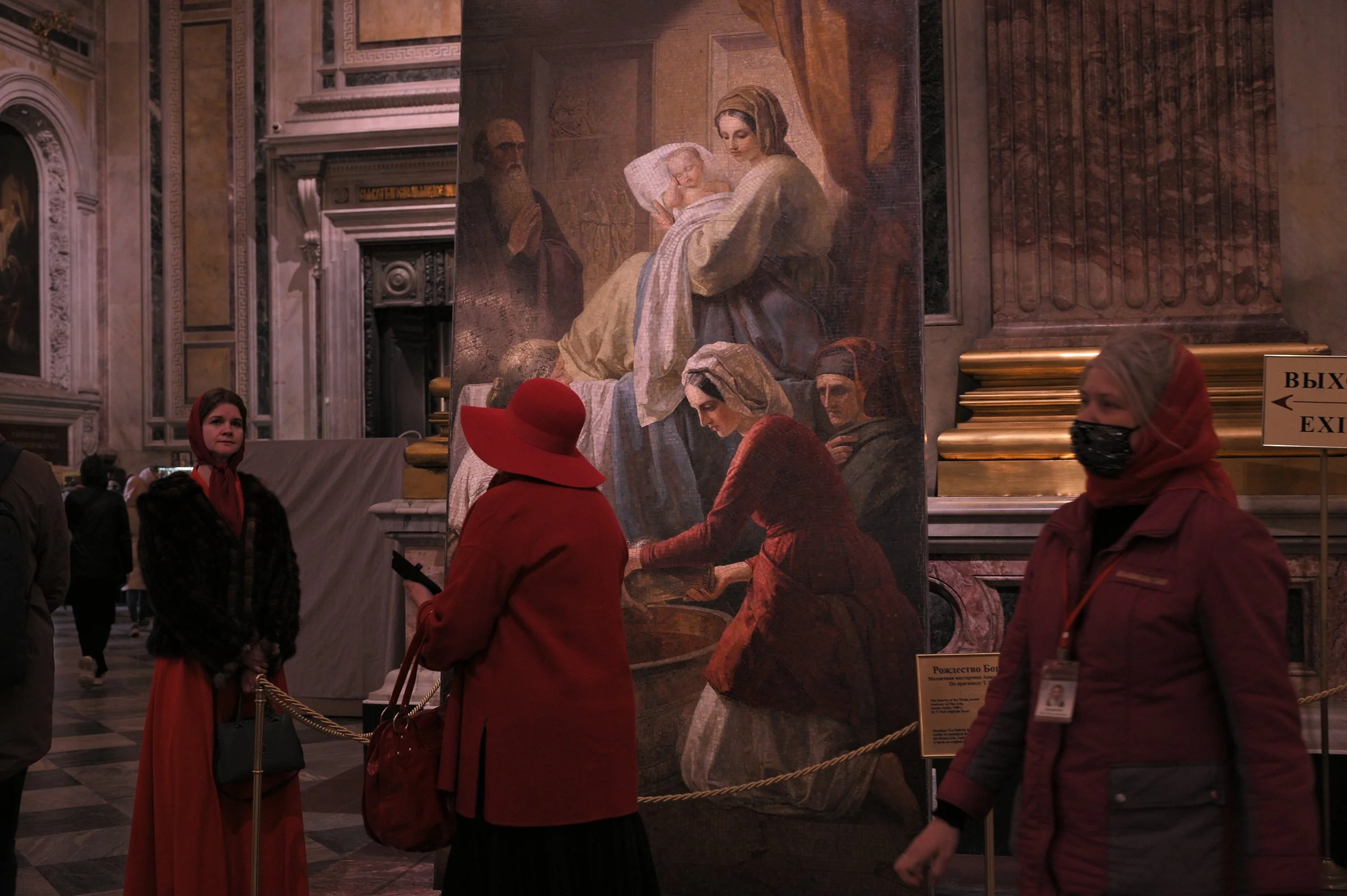 People inside a museum viewing a large religious-themed painting showing a woman holding a child, with other figures around her.