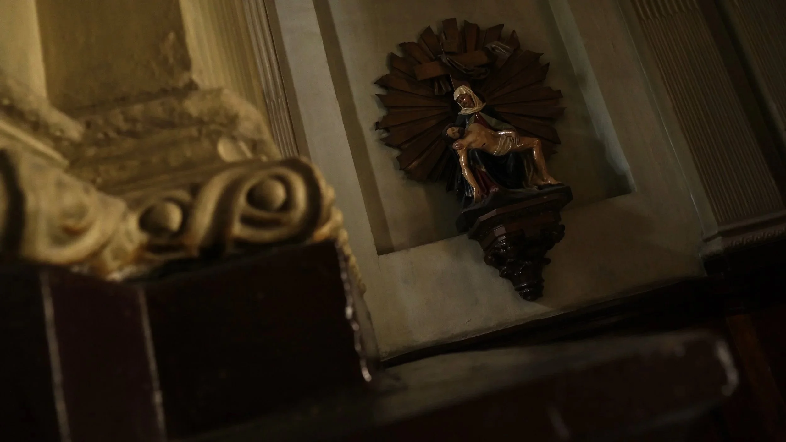 Religious statue of Jesus Christ after being taken down from the cross, installed on a wall in a church or chapel, with a decorative wooden backdrop.