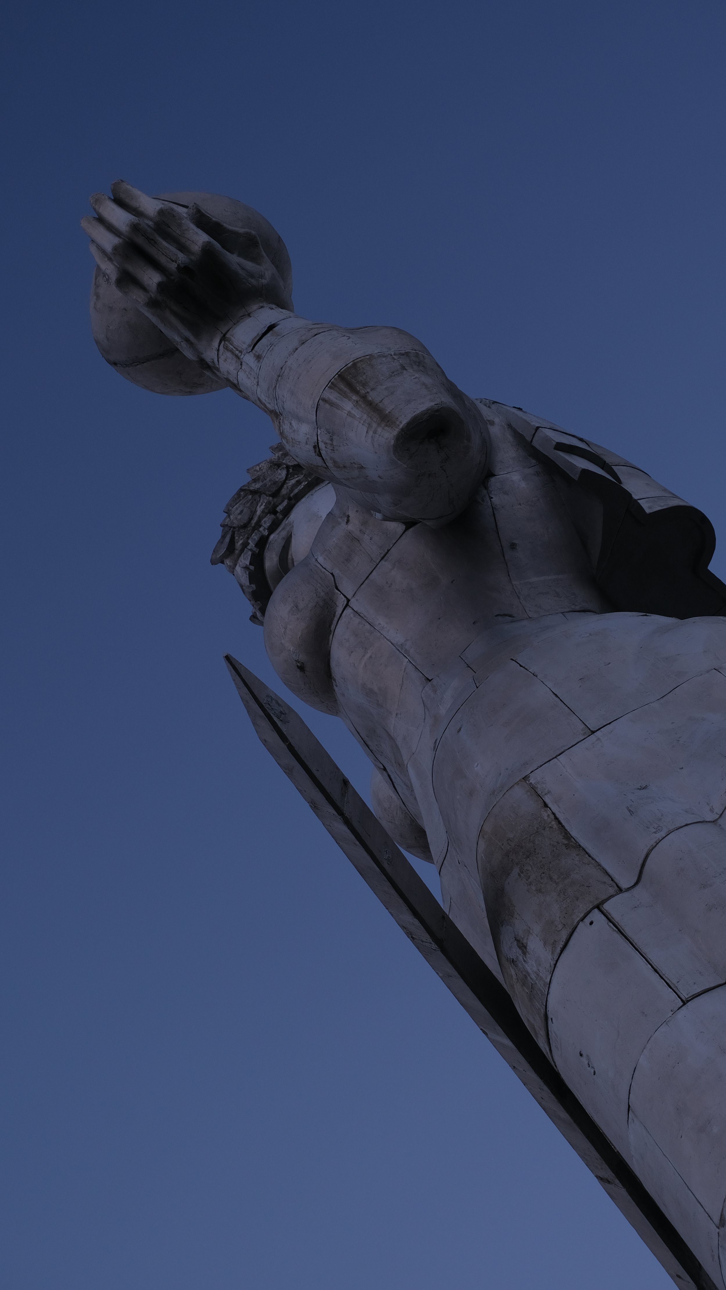 Low-angle view of the The Motherland Statue in Tbilisi against a dark blue sky.