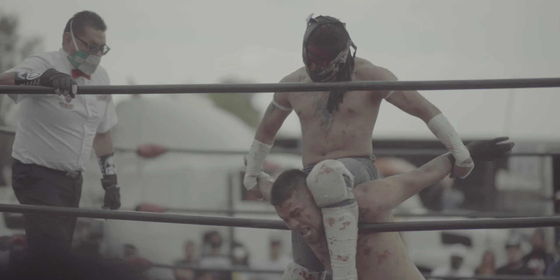 Boxers in a match, with one boxer on the ground and another sitting on his shoulders, during a match at a boxing ring.