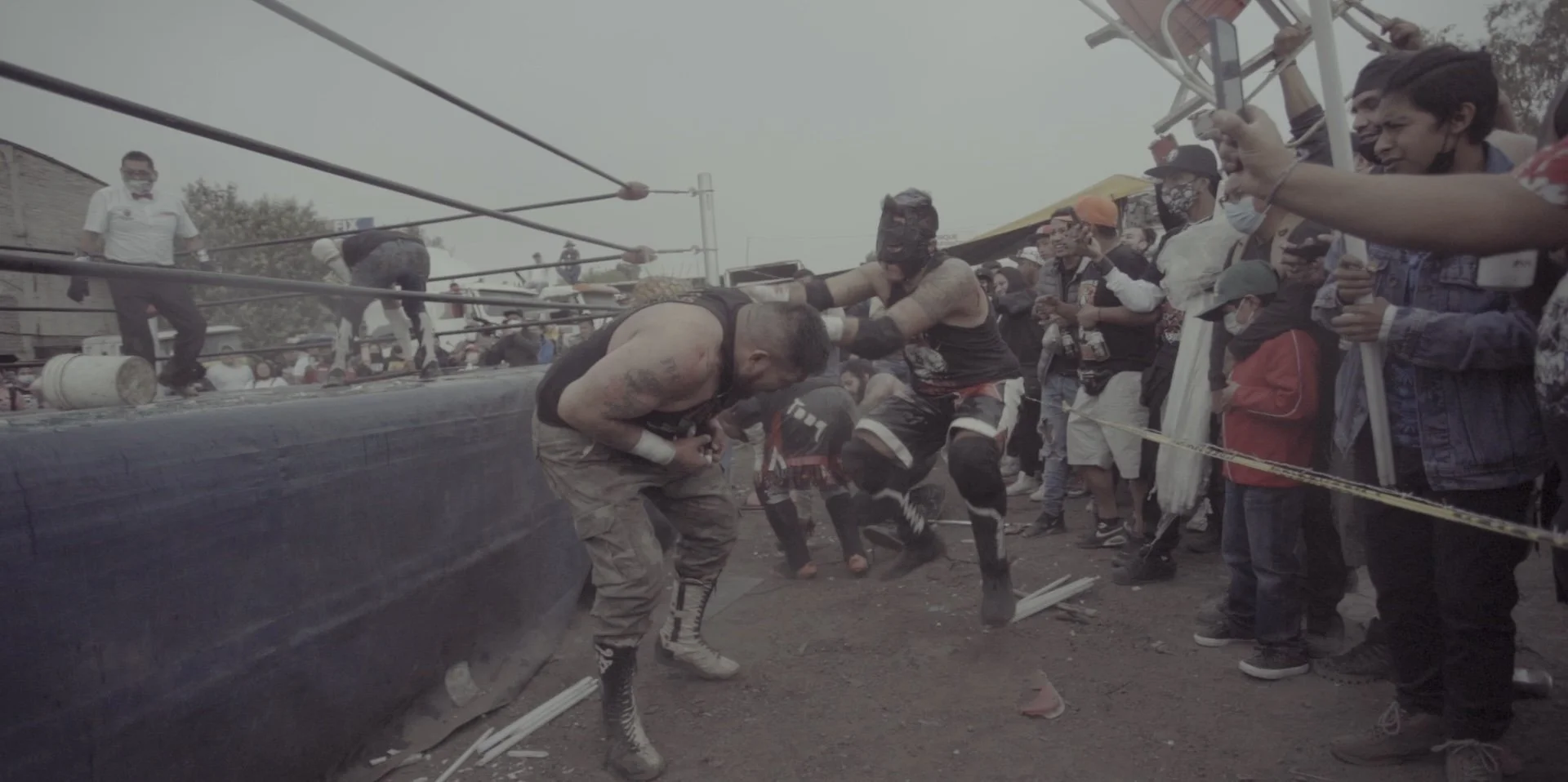 Two wrestlers fighting inside a wrestling ring, surrounded by spectators watching and recording the match.