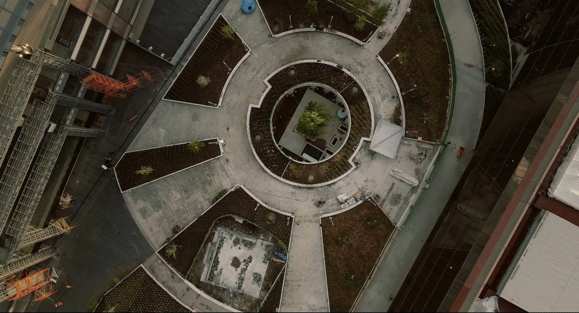 Aerial view of a circular rooftop garden with pathways, small trees, and planters on a high-rise building.