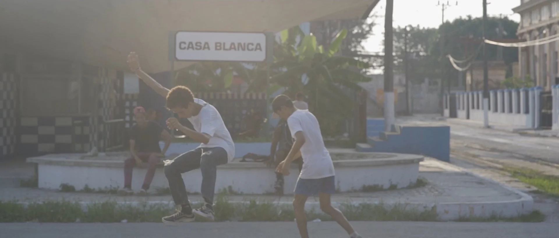 Three boys playing on a street in front of a building with a sign reading 'Casa Blanca', during sunset or early evening.