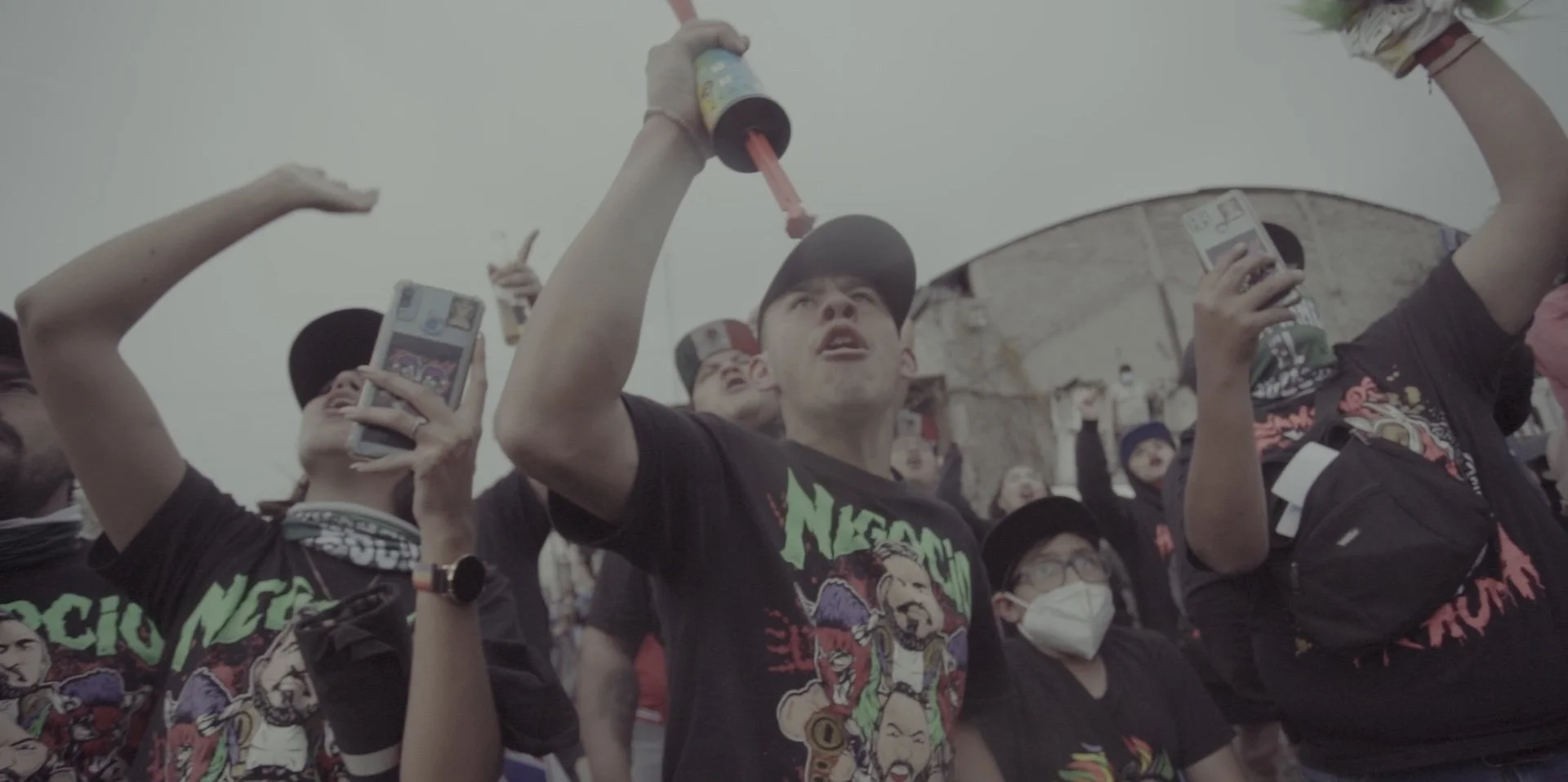 A group of young people at a protest, some taking photos, holding posters, and lifting their fists in the air.