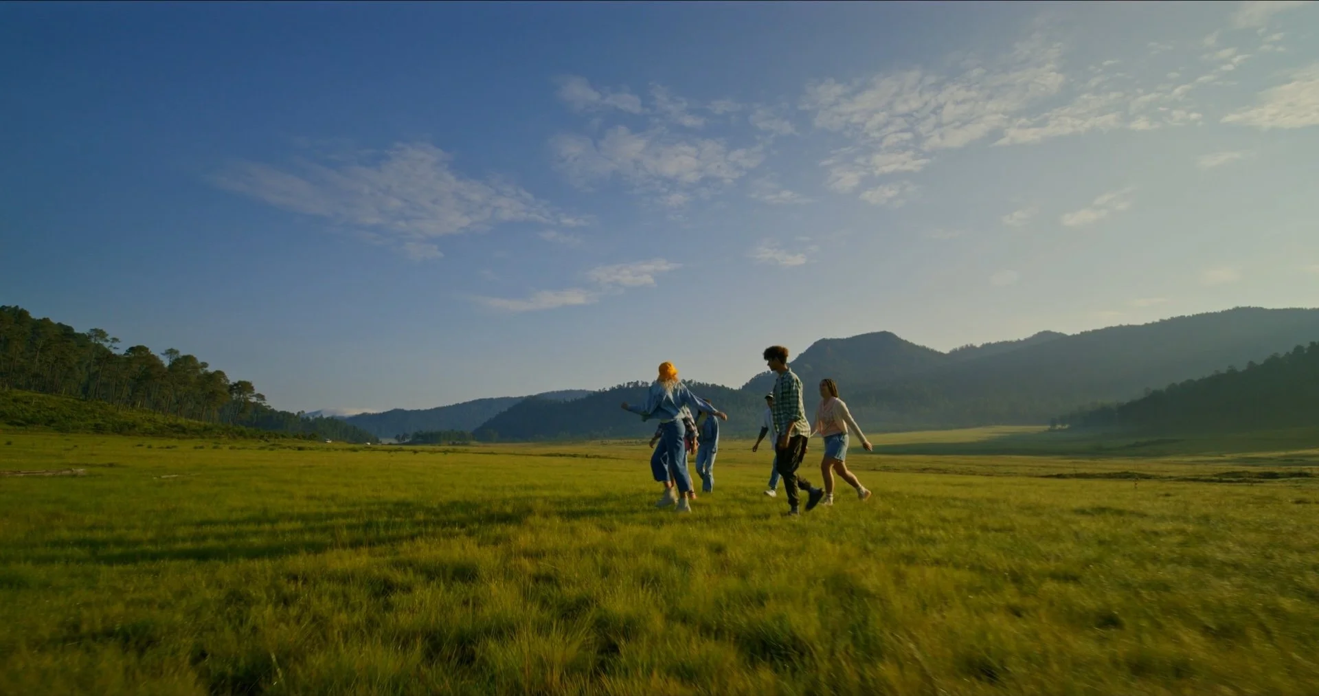 A group of five people walking on a grassy field with mountains in the background under a partly cloudy sky during daytime.