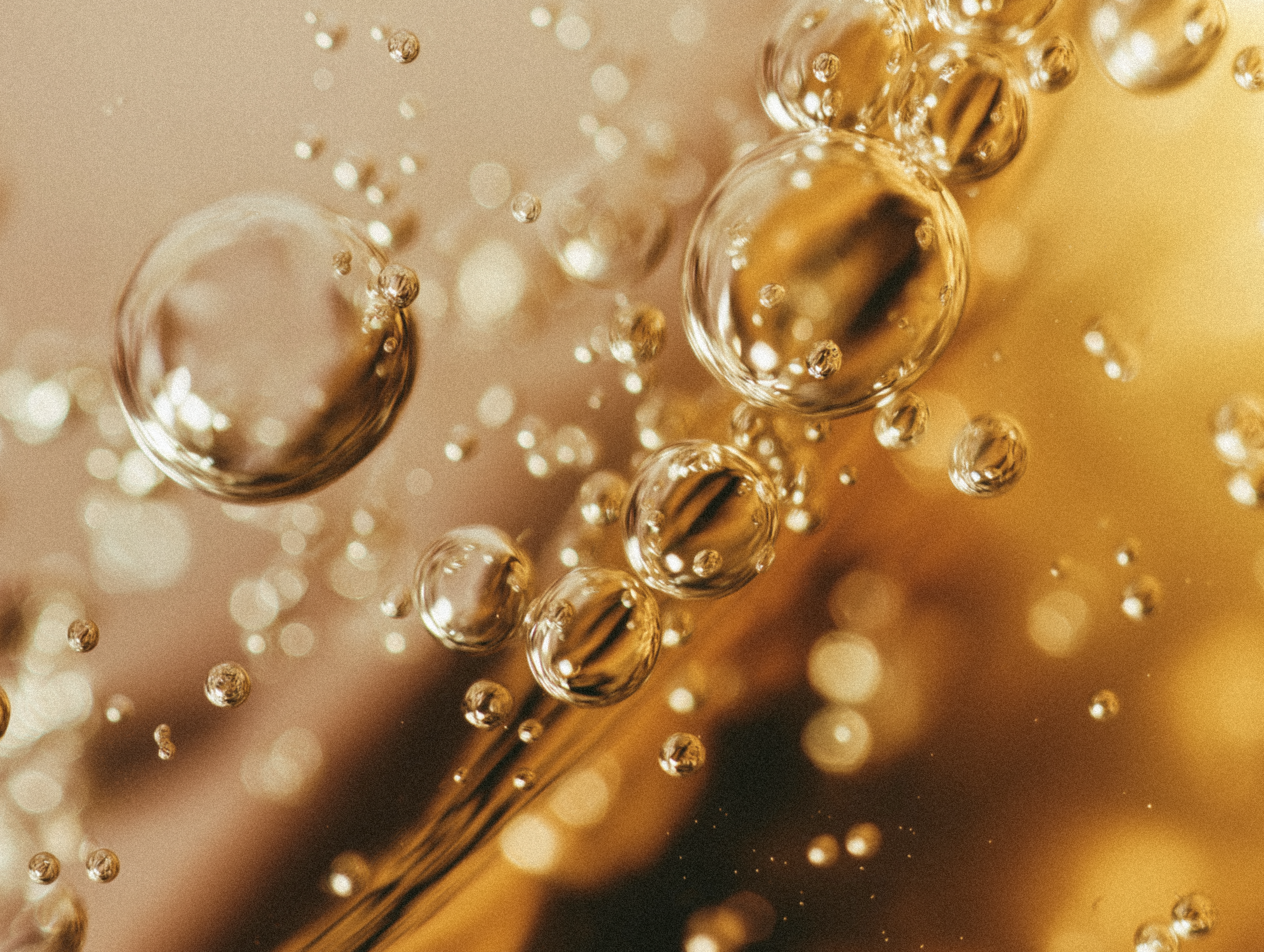 Close-up of bubbles in beauty oil, with golden tones and reflections.