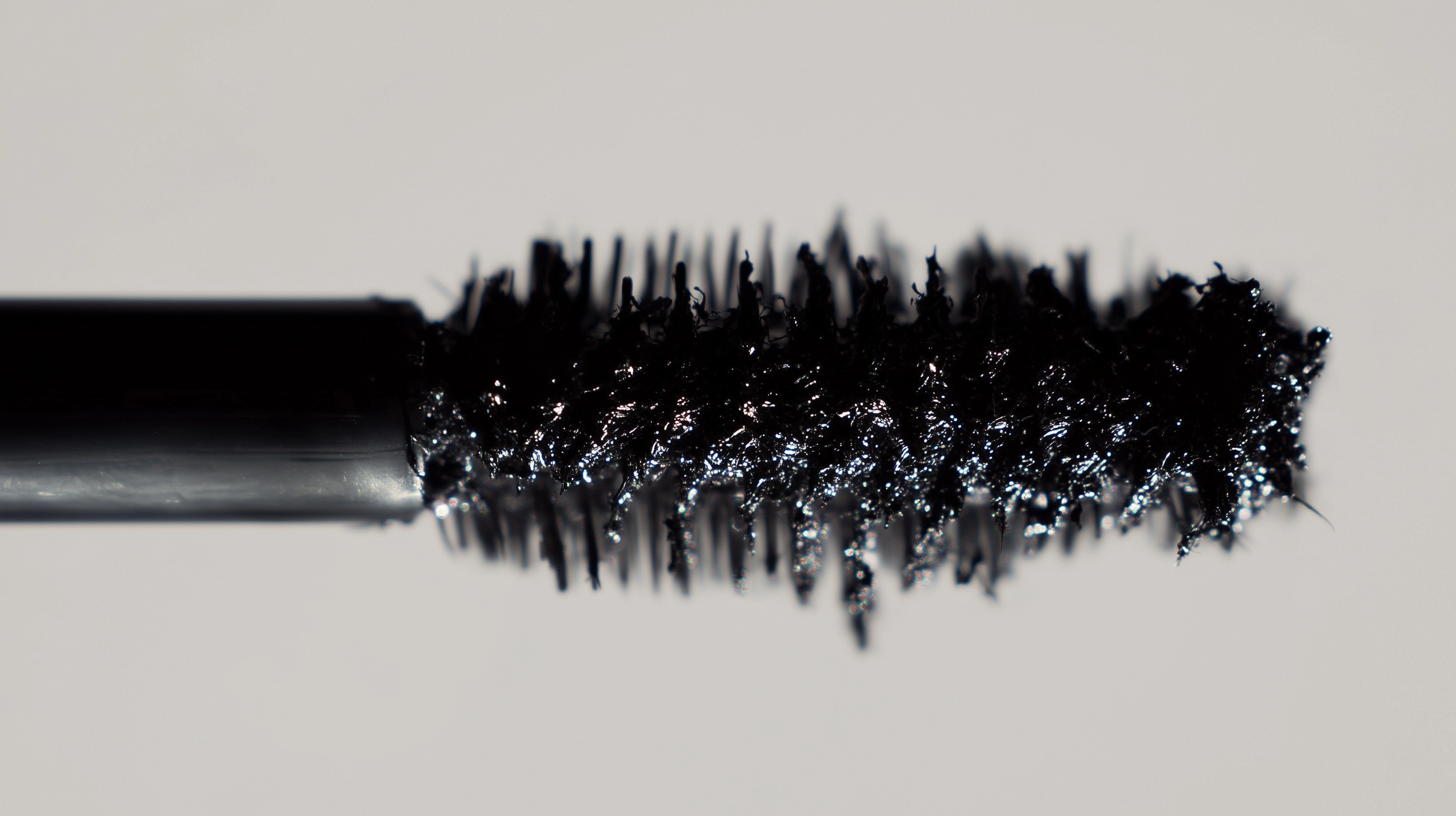 Close-up of a black mascara wand coated with mascara, showing the bristles and product texture.