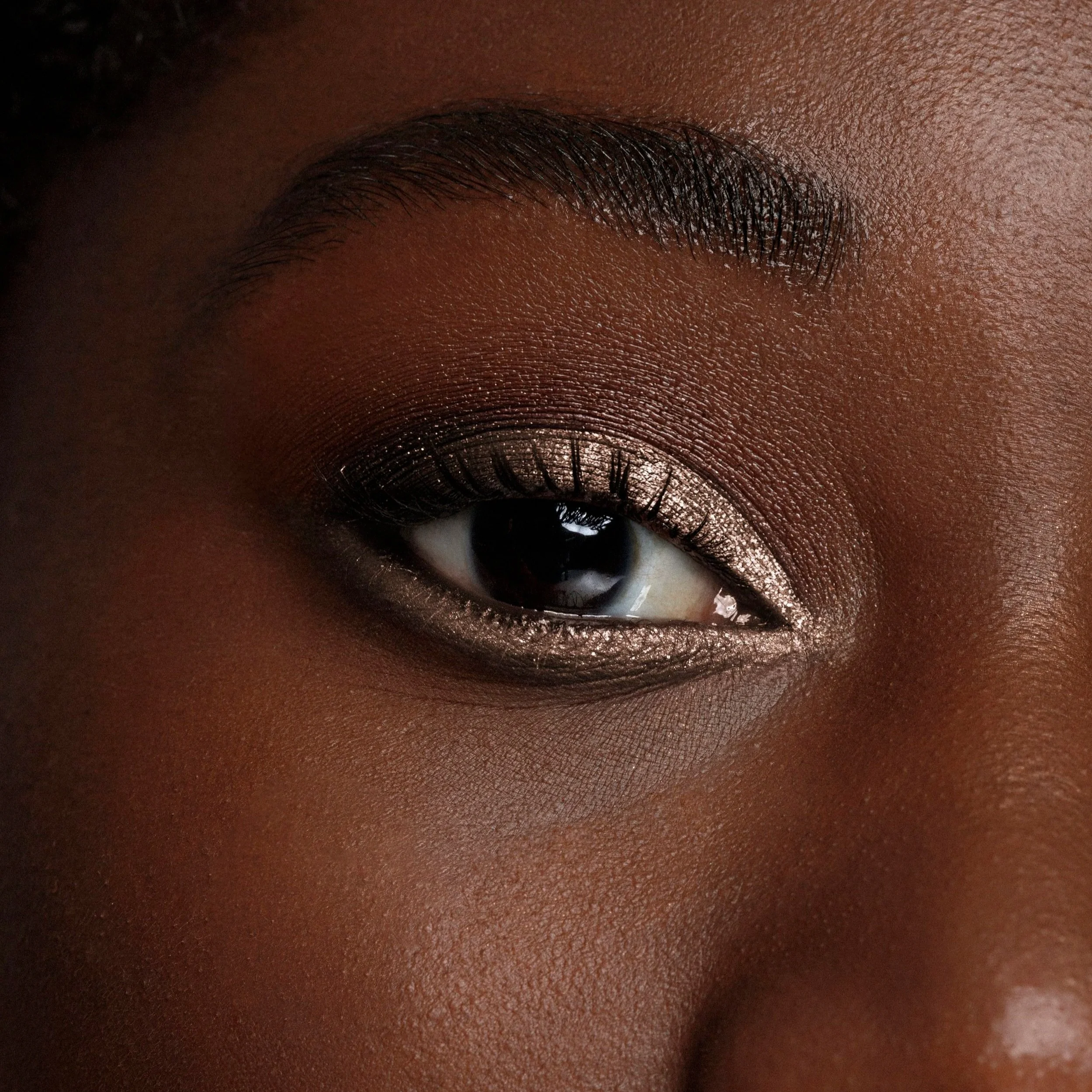 Close-up of a woman's eye with shimmery nude eyeshadow, defined eyebrow, and smooth skin.