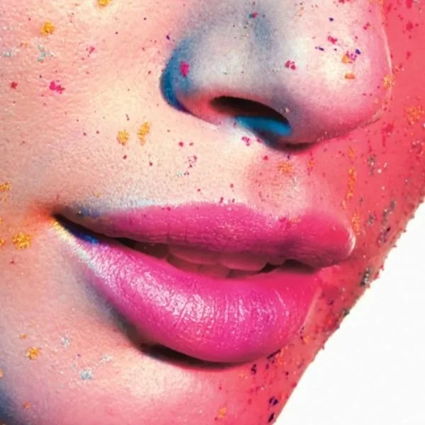 Close-up of a person's lips and nose with colorful glitter and makeup on the face, pink lipstick, and blue eyeshadow near the nostrils.