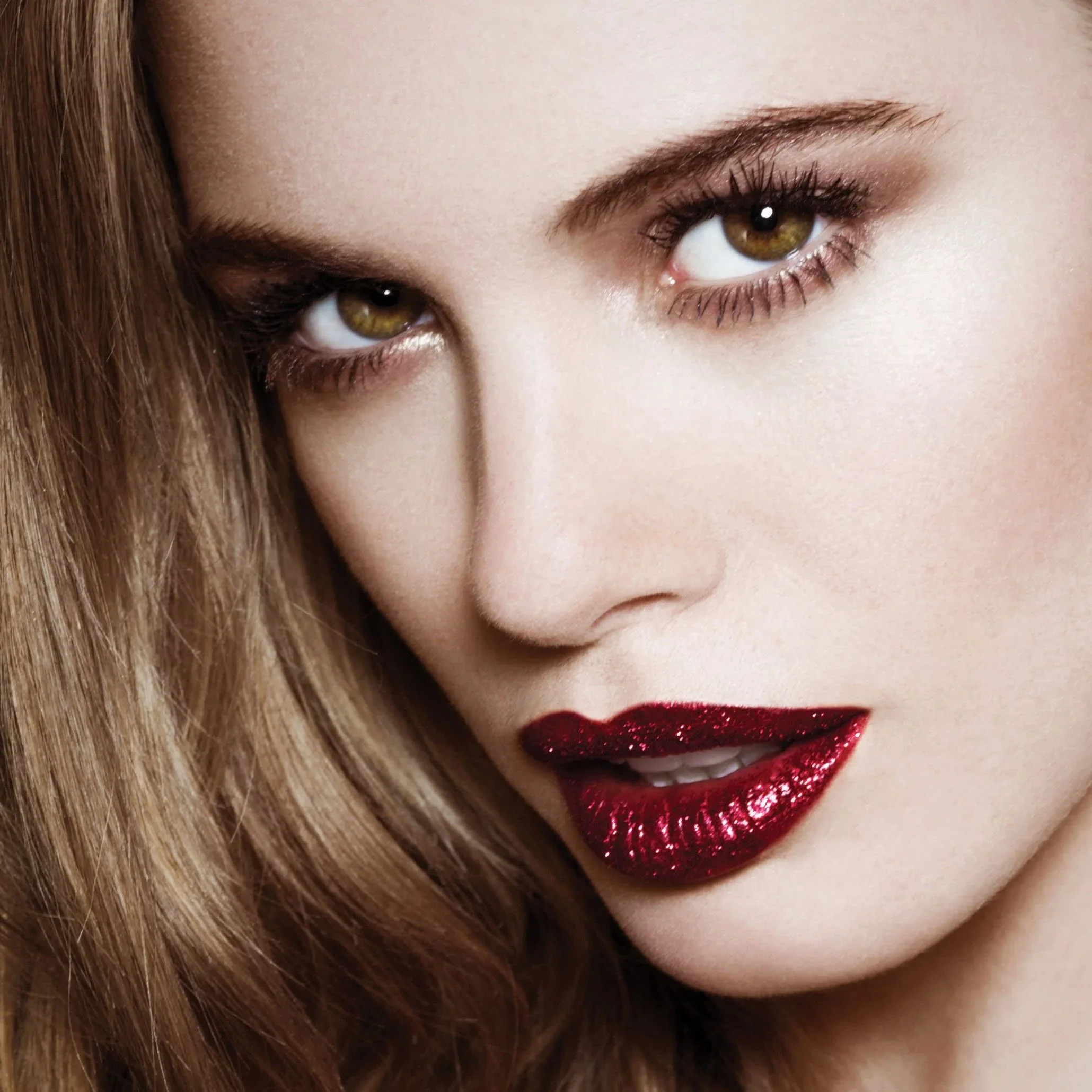 Close-up of a woman's face with red lipstick and eye makeup, looking directly at the camera.