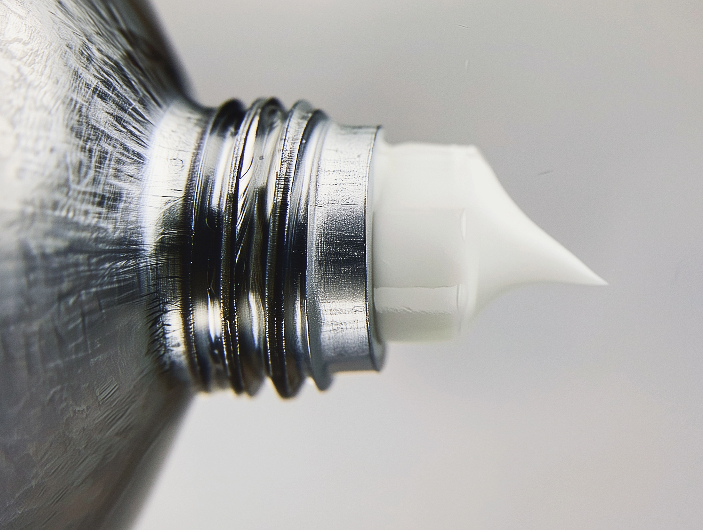 Close-up of a metal screw with threads, partially inserted into a white plastic object against a plain background.