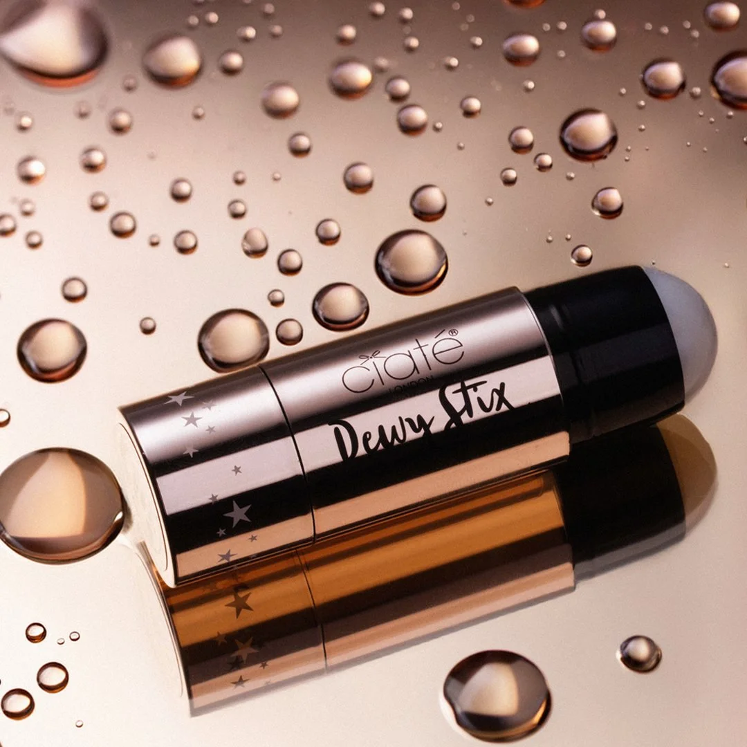 A metallic vaporizer labeled 'Dewy Stix' resting on a reflective surface with water droplets scattered around.