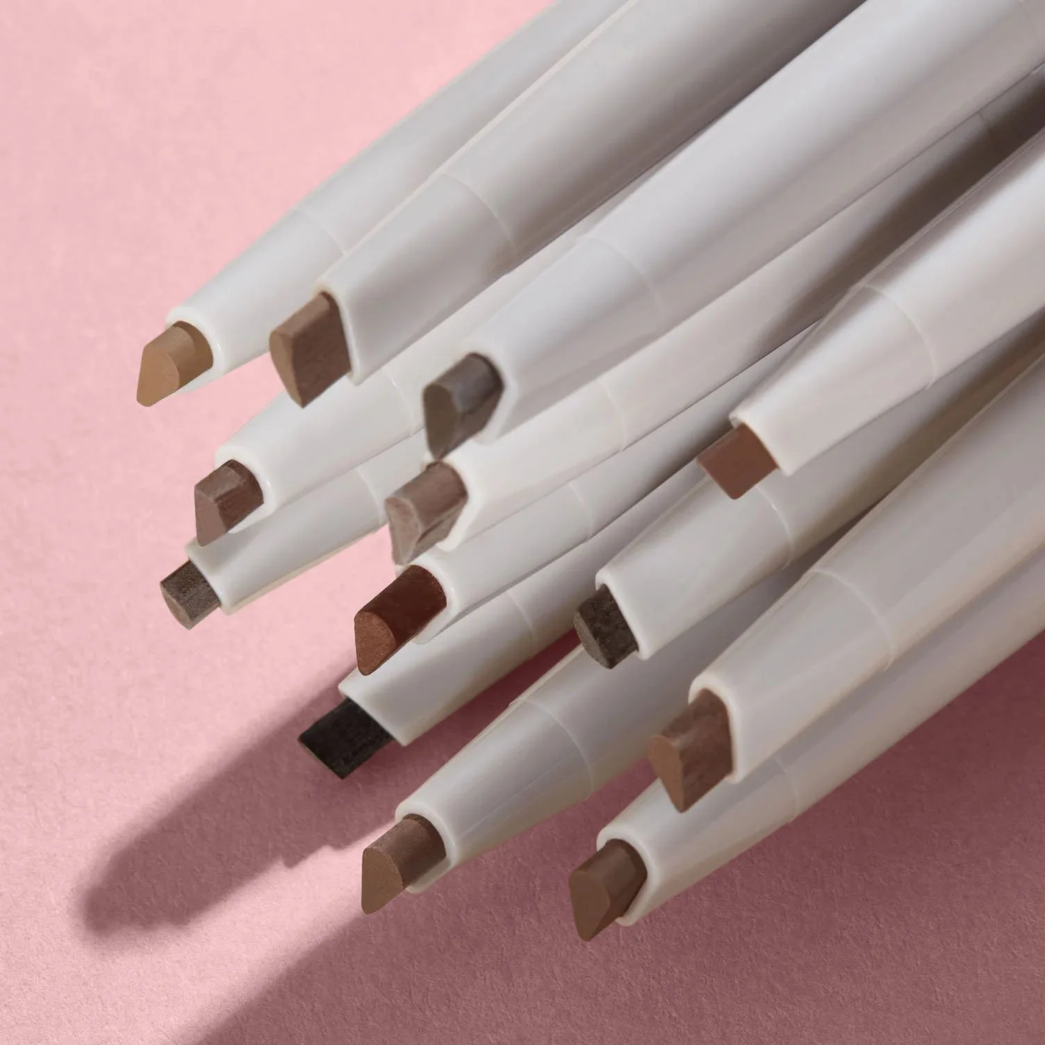 Close-up of  eyebrow pencils, arranged on a pink surface.