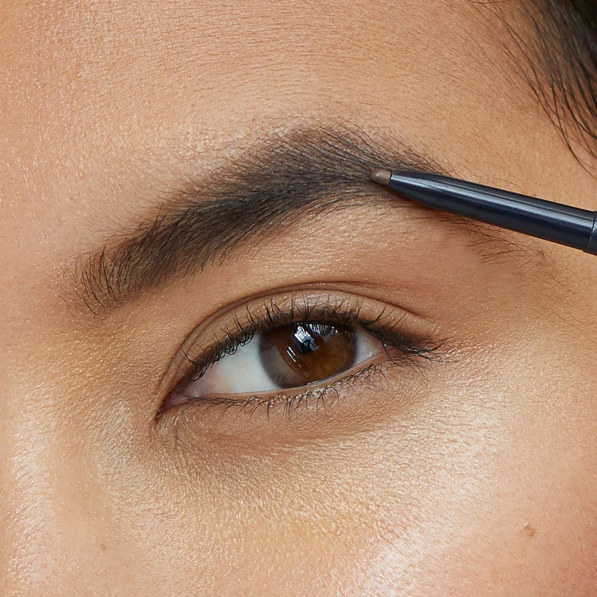 Close-up of a person applying makeup to their eyebrow with an eyebrow pencil.