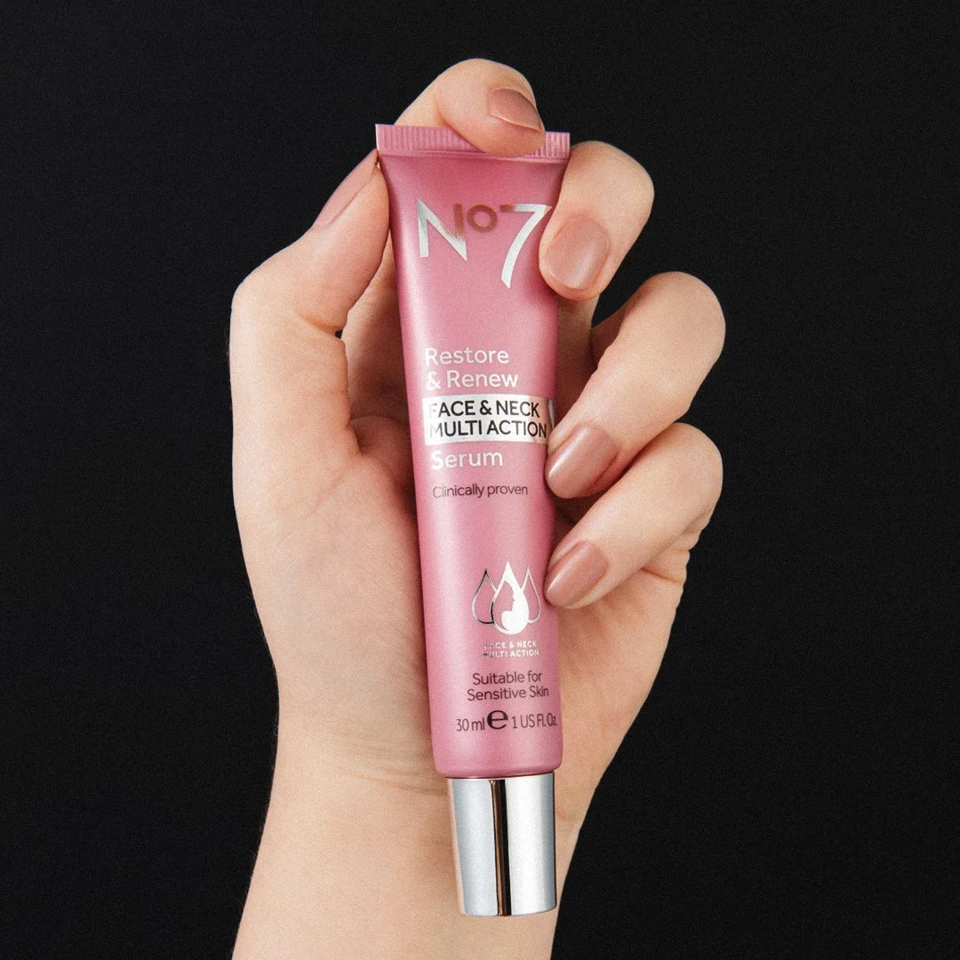 A hand holding a pink tube of N°7 Restore & Renew Face & Neck Multi Action Serum.