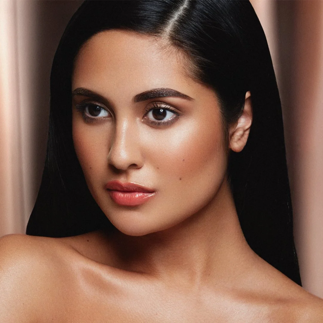 Close-up of a woman with long black hair, natural makeup, and a smooth complexion, looking slightly to the side with a neutral expression.