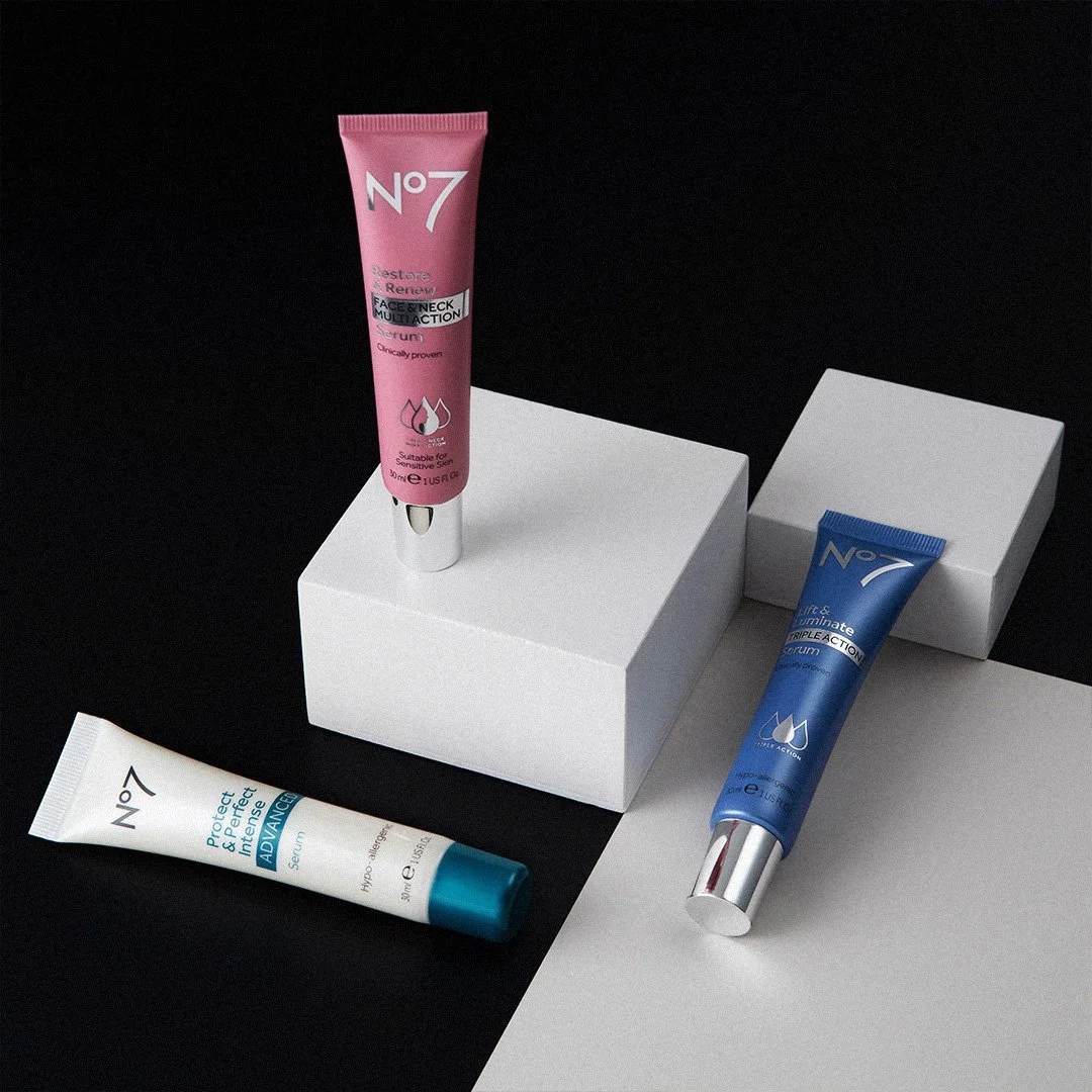 Three tubes of skincare serums in different colors, pink, blue, and white, placed on white blocks and a black background.