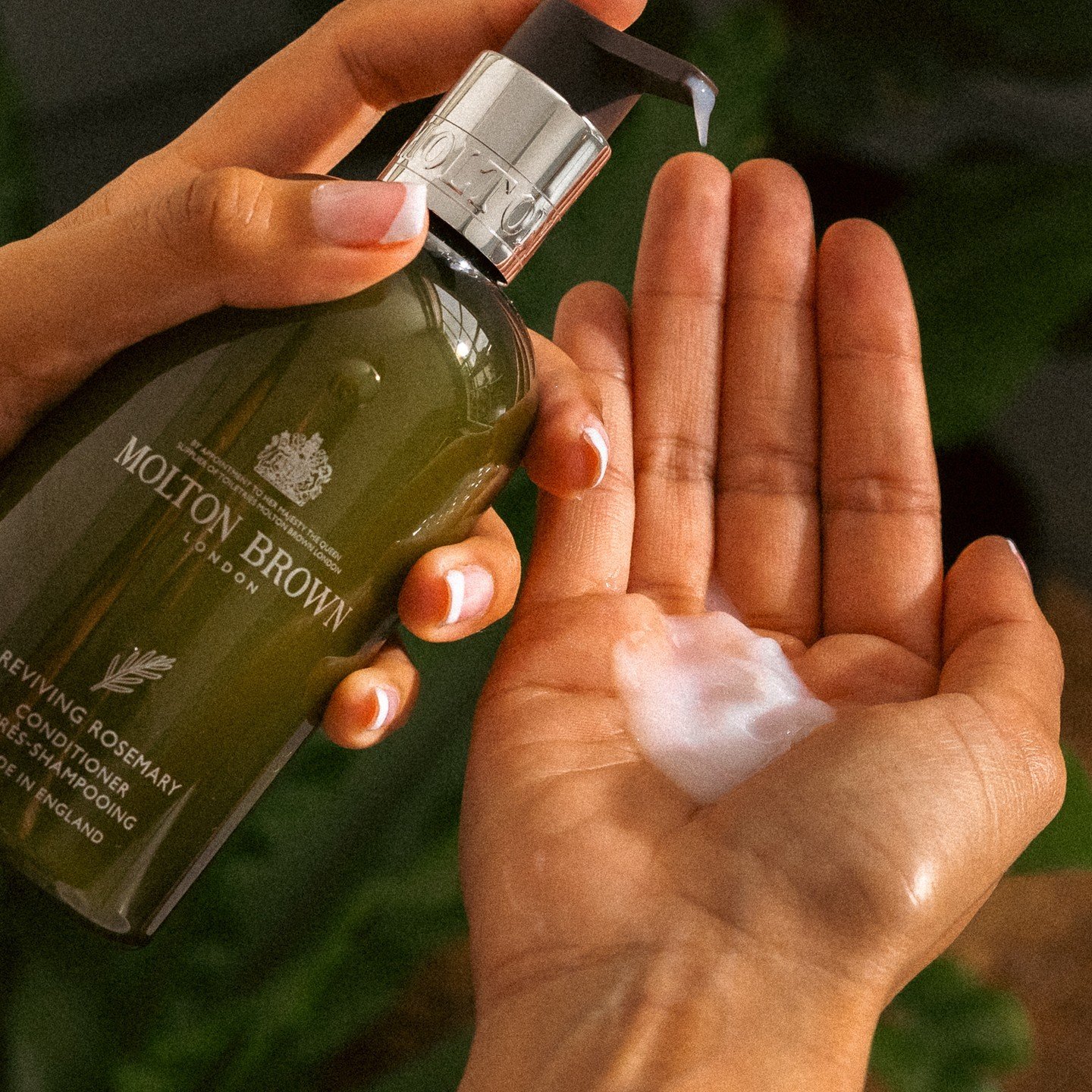 Person applying moisturizer or lotion from a green bottle labeled 'Molton Brown London' onto their palm.