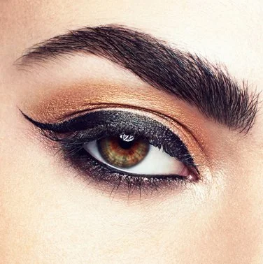 Close-up of a woman's eye with dramatic gold and black eye makeup and a bold black eyeliner.