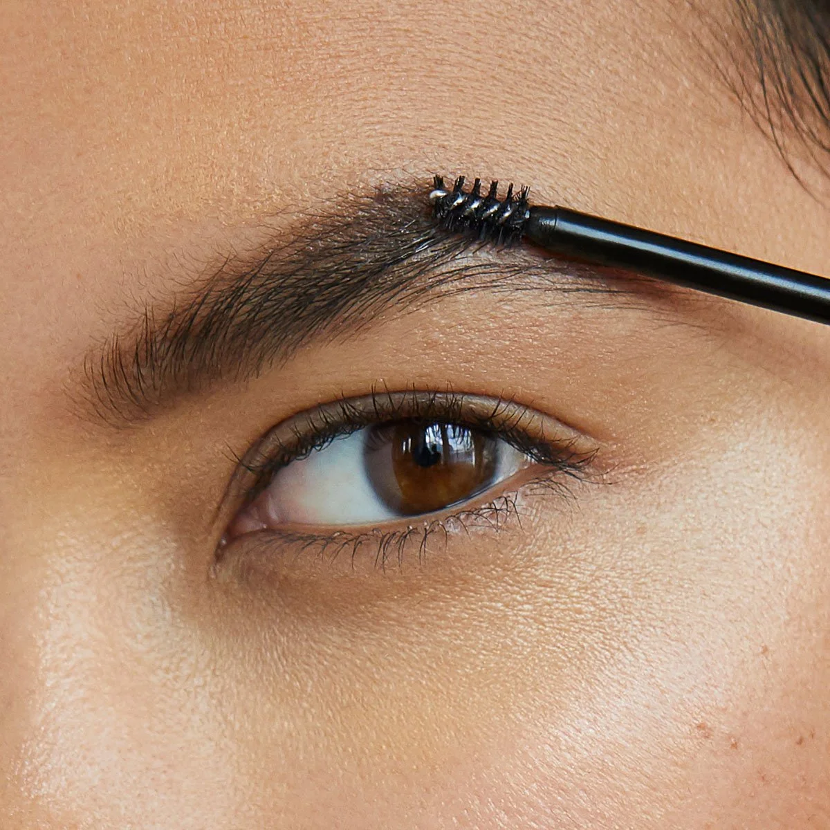 Close-up of a person's eye with a brush applying eyebrow gel on the eyebrow.