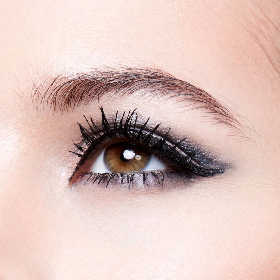 Close-up of a person's eye featuring brown iris, black eyeliner, mascara, and eyeshadow, with well-groomed eyebrow above.