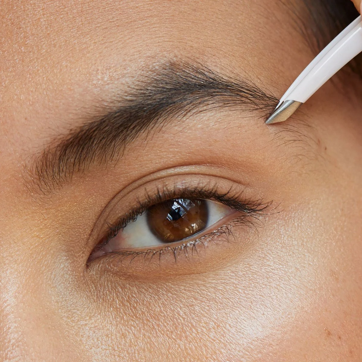 Close-up of brow grooming using tweezers