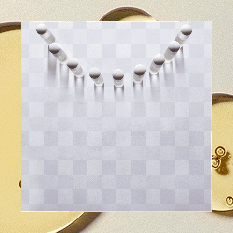 Marbles lined up on a sheet of paper with shadows cast on a surface.
