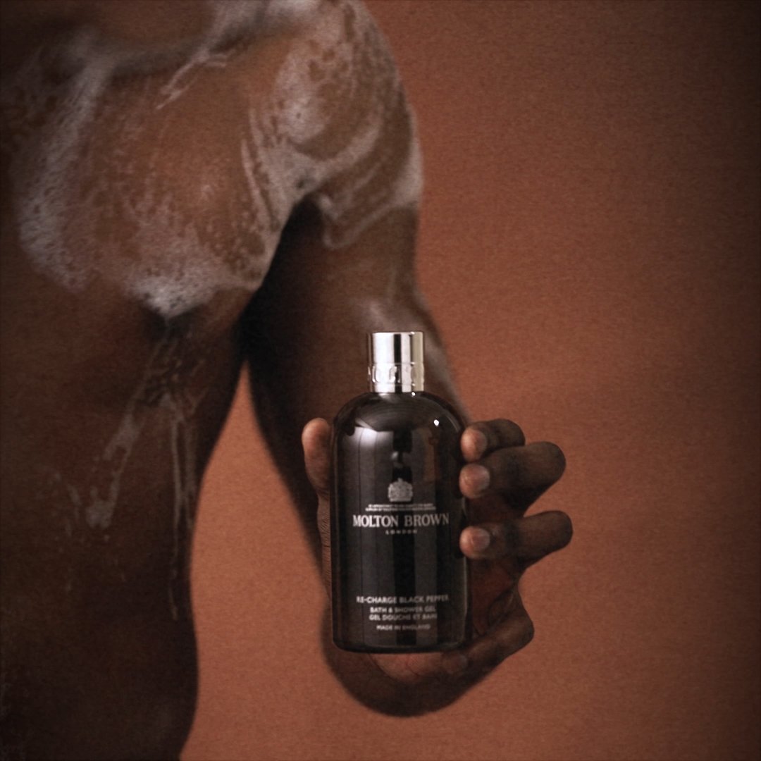 Hand holding bodywash bottle against deep brown background