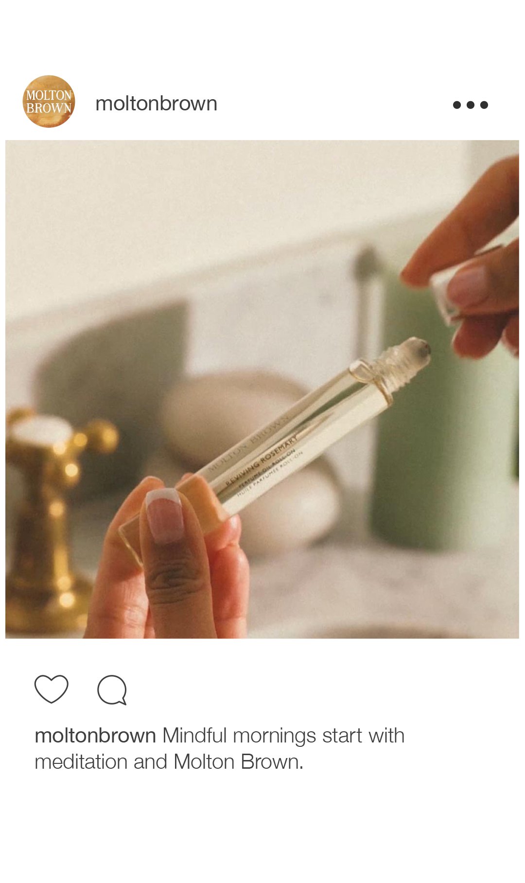 A person holds a small glass tube labeled 'LEMON AND ROSEMARY' with a white essential oil or perfume inside, with a blurred background of home decor items.