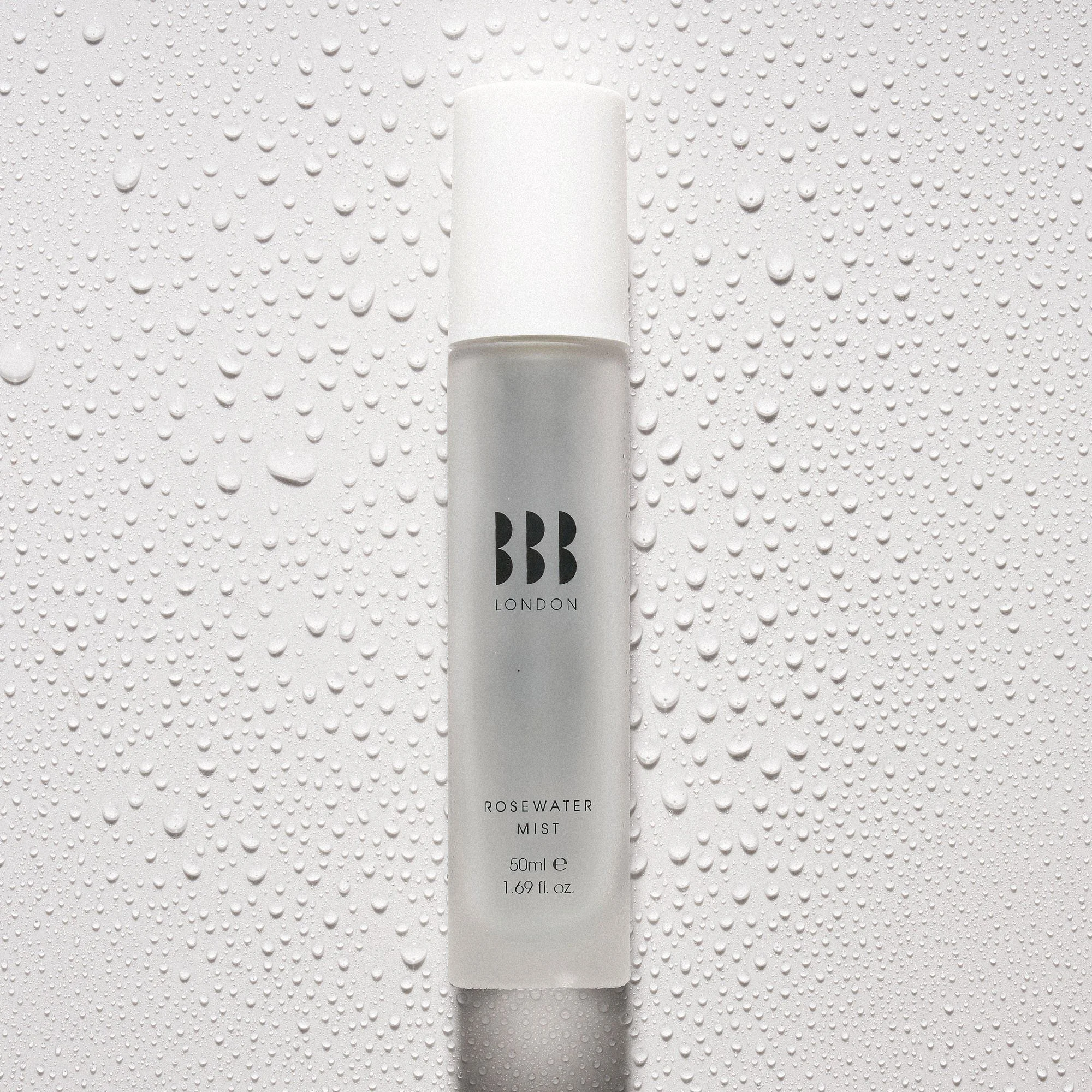 A white bottle of BB London Rosewater Mist with water droplets on the surface and background.