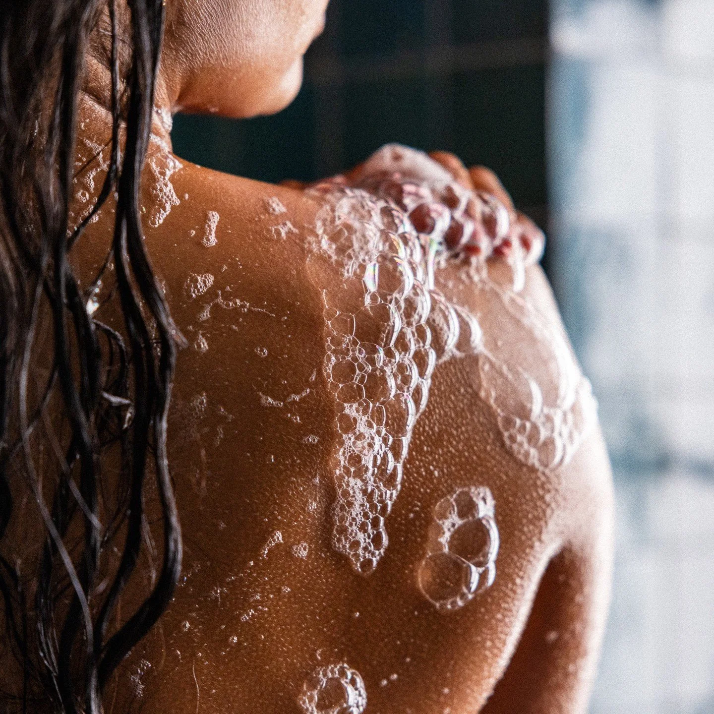 Close-up of a person's back with wet hair and soap bubbles on their skin.