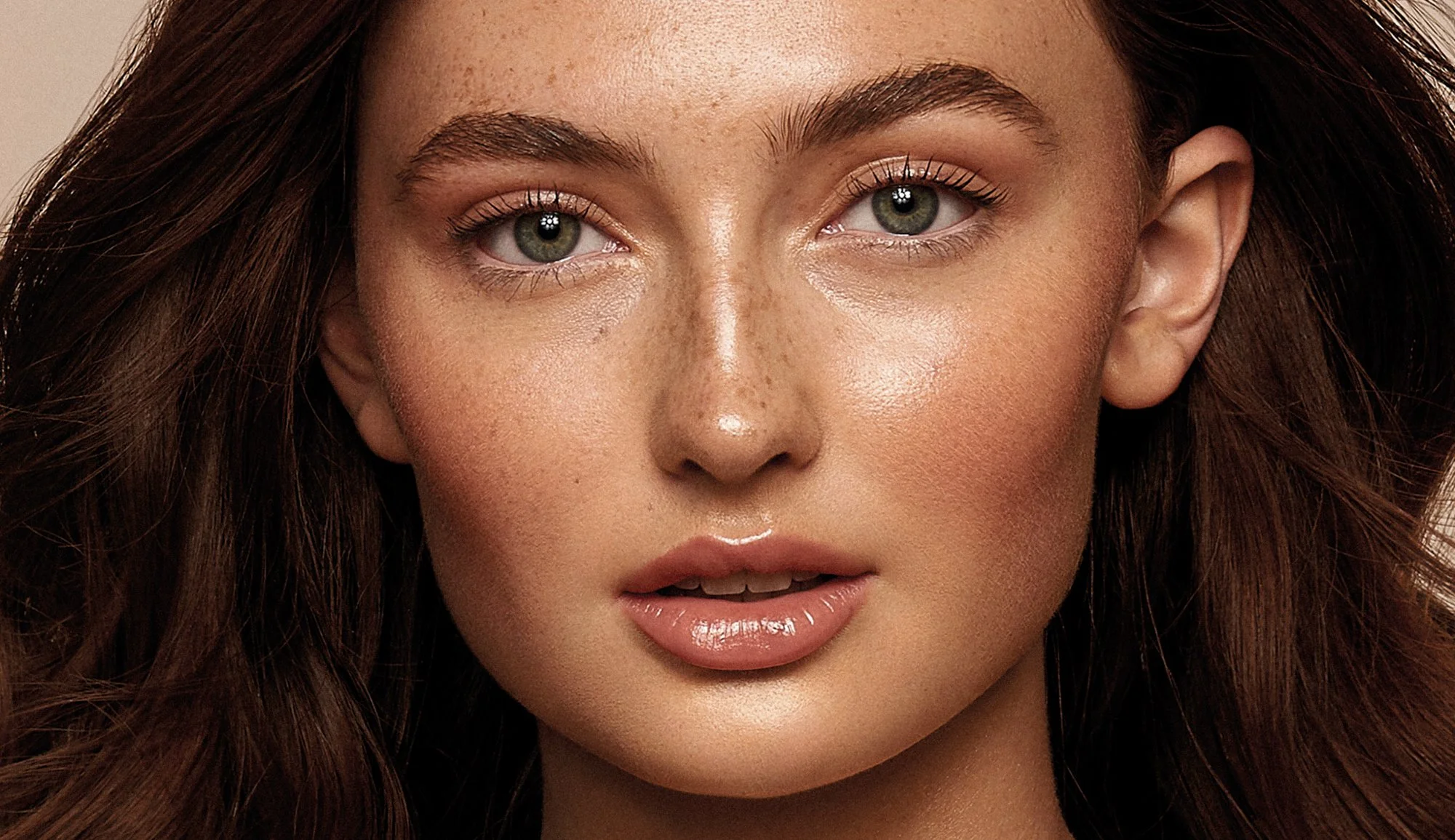 Close-up editorial beauty portrait of a woman with long brown hair, light makeup, and green eyes
