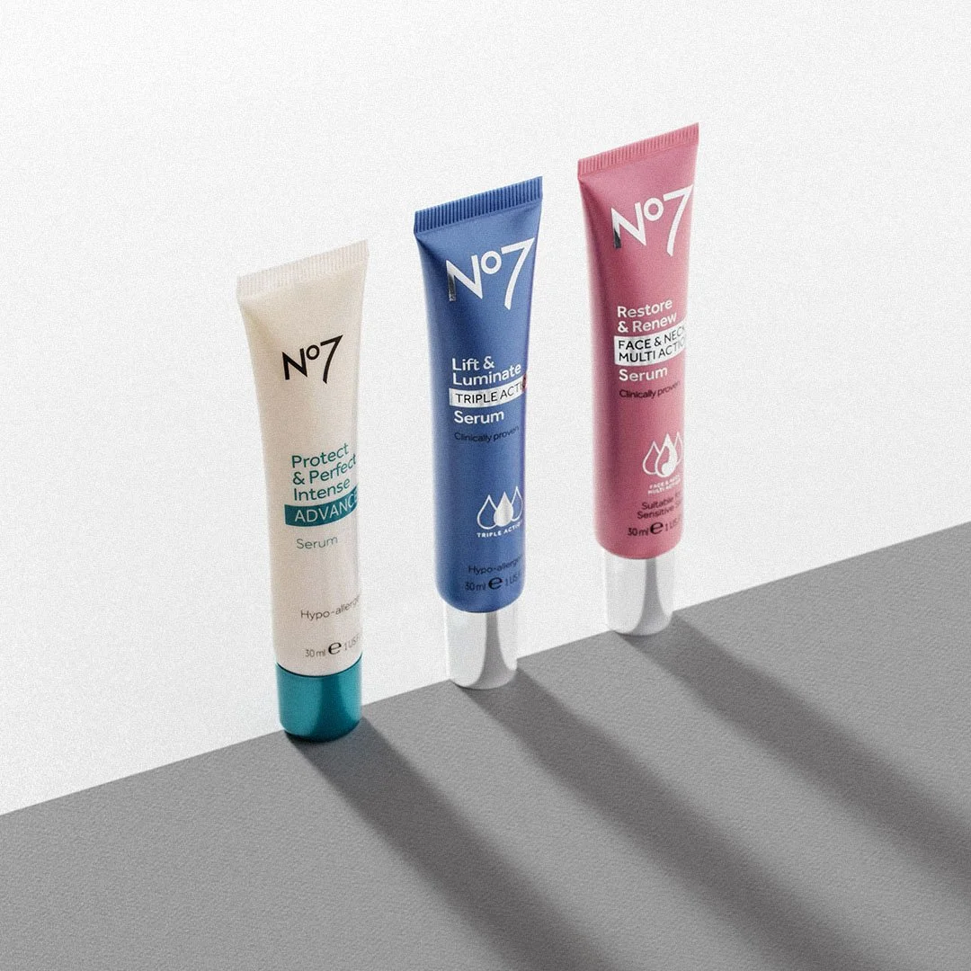 Three tubes of skincare serum standing on a gray surface with shadows, featuring labels for different skin benefits and ingredients.