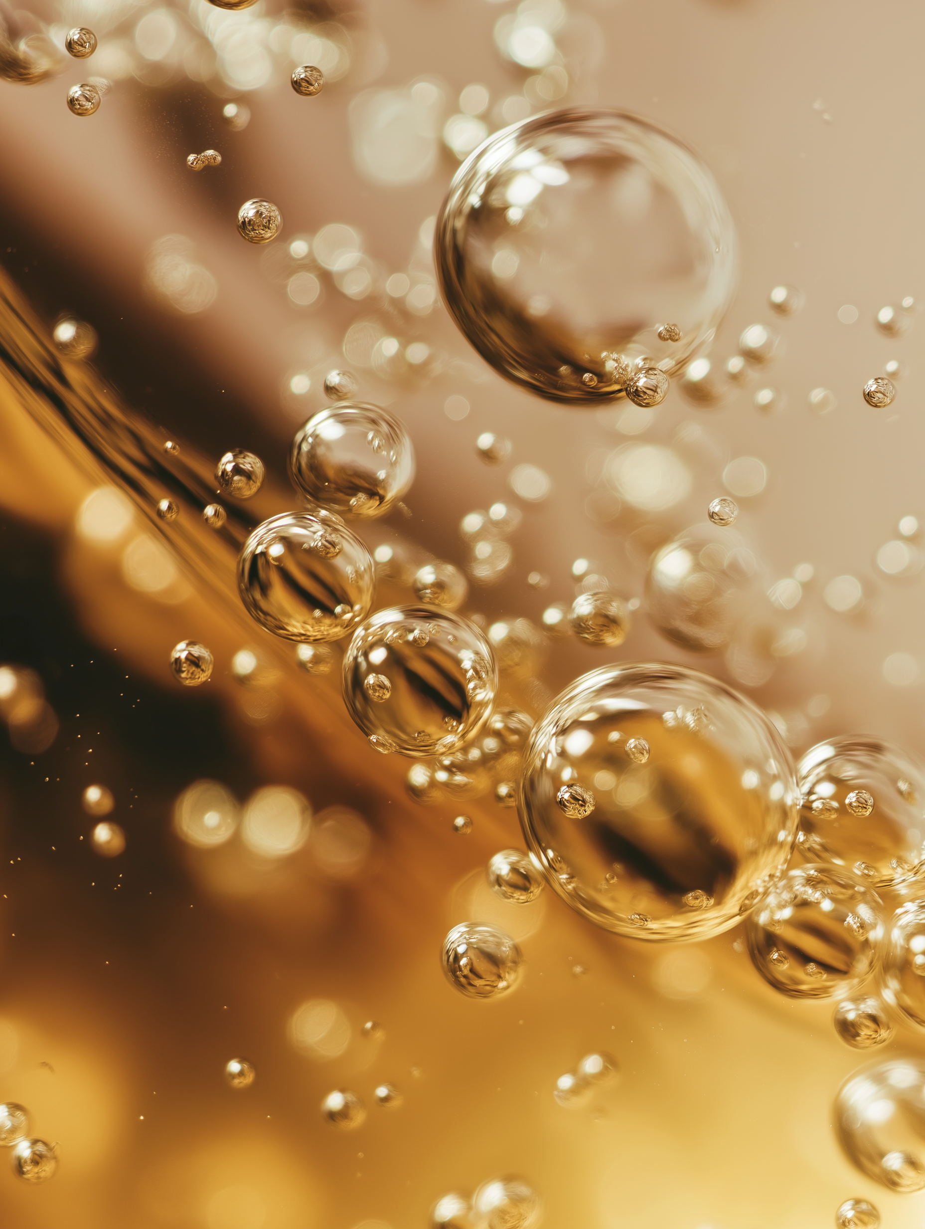 Close-up abstract of bubbles or tiny particles in a golden liquid, with sparkling reflections and a warm golden background.