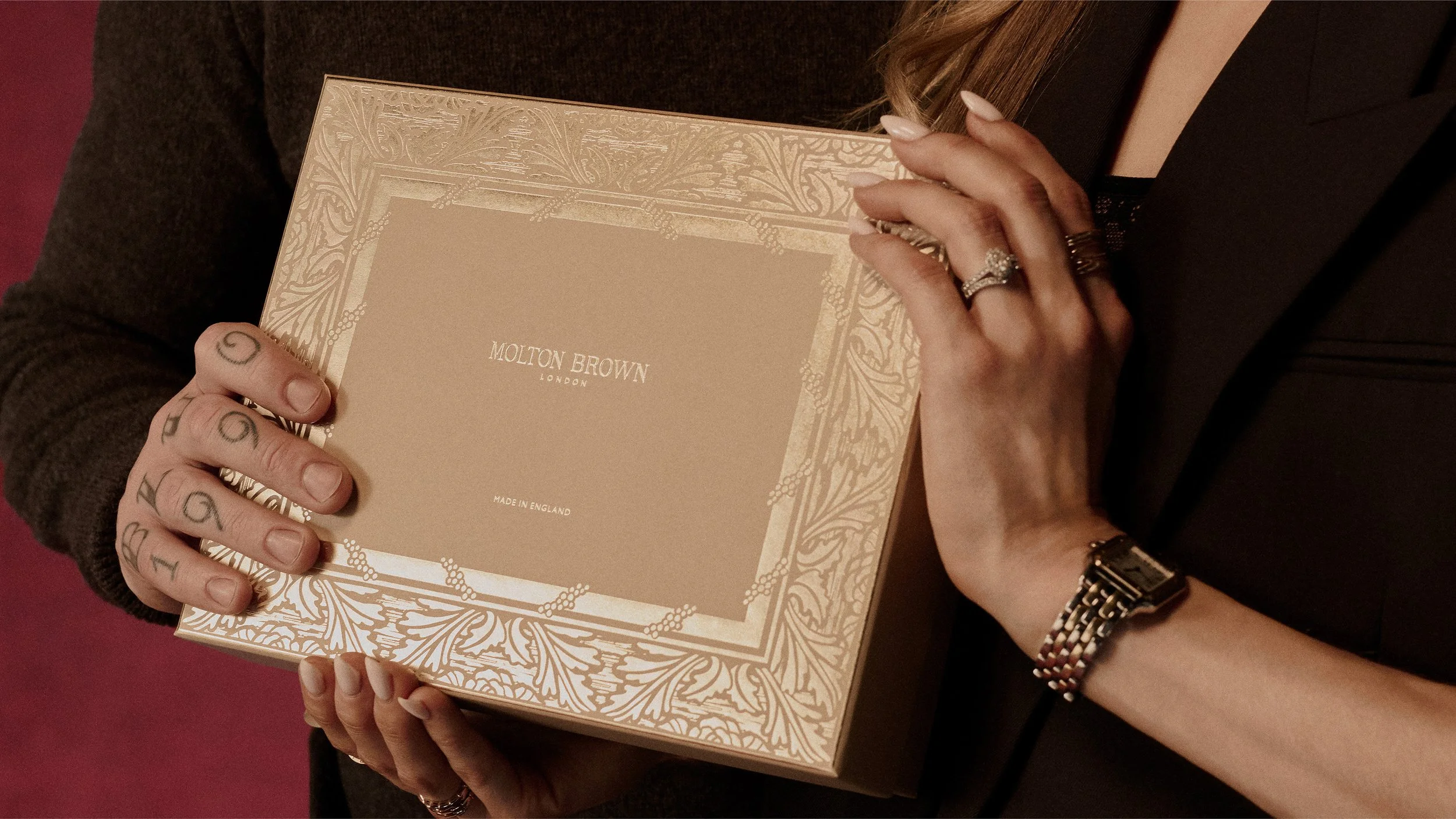 Hands holding Molton Brown gift box in Christmas gifting campaign still, highlighting tactile packaging and premium finish.