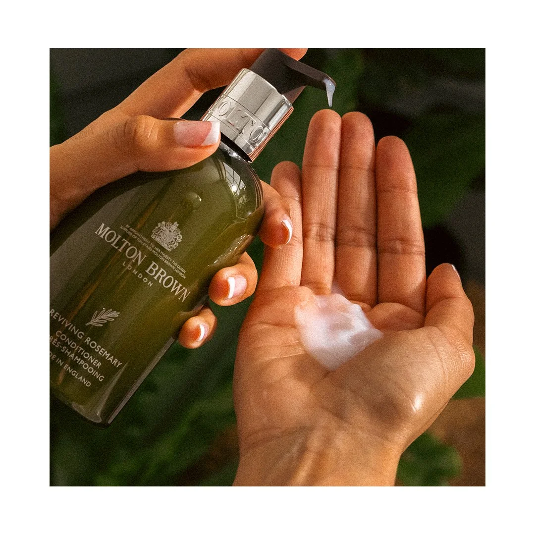 Person dispenses lotion from a Molton Brown Rosemary hand cream bottle onto their palm.