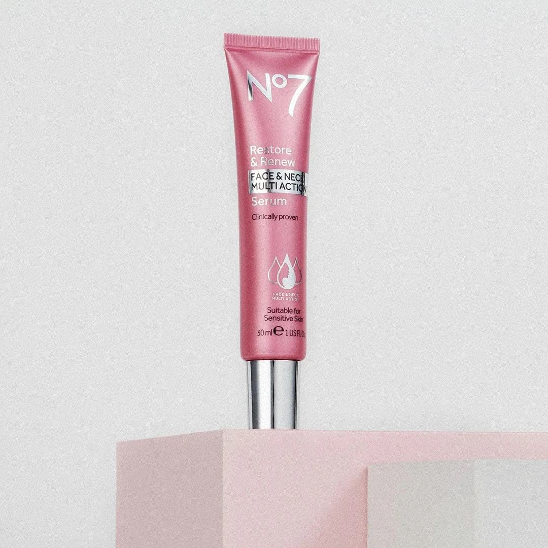 Pink tube of No7 Restore & Renew Face & Neck Multi Action Serum standing upright on a pink block against a plain background.