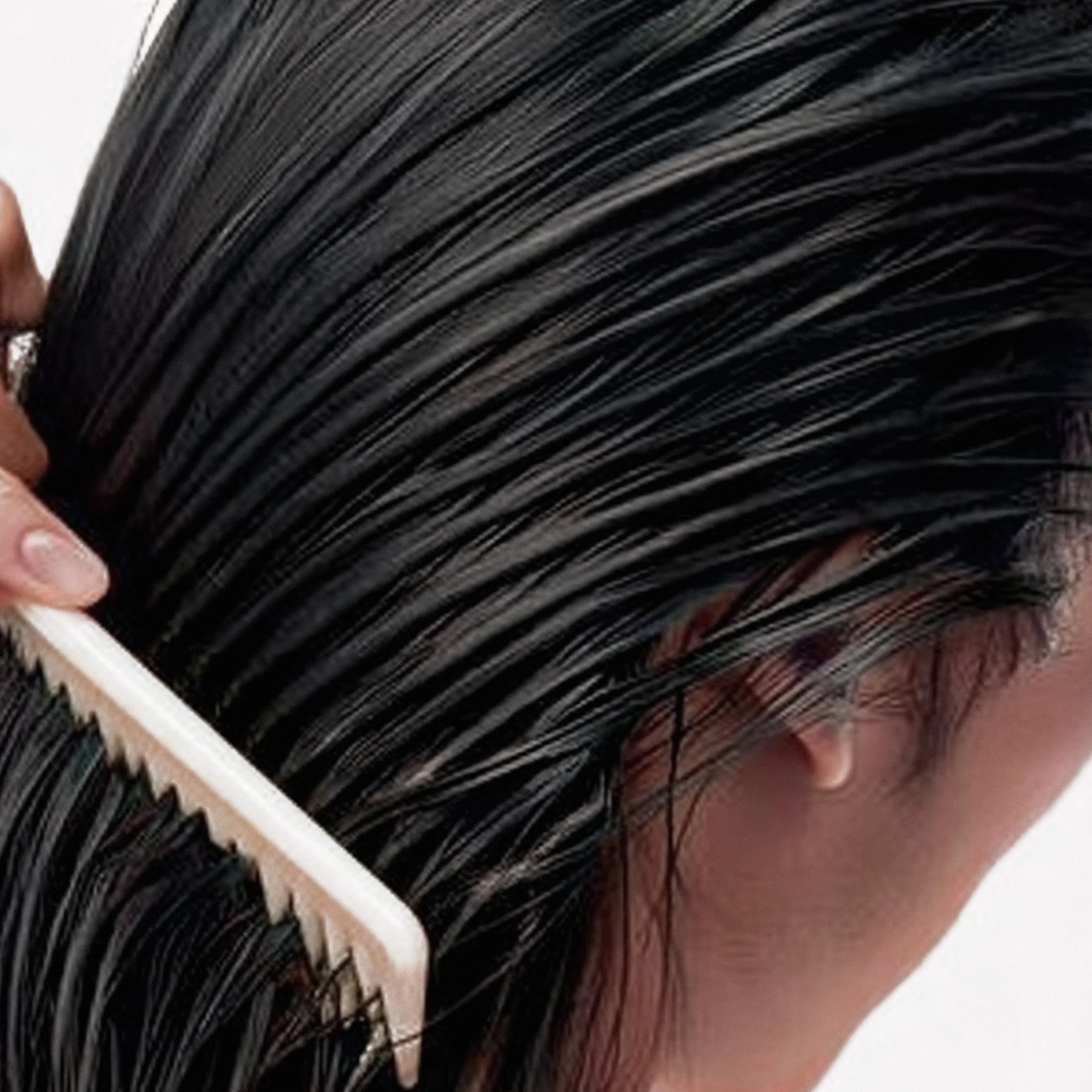 Close-up of a person with wet, dark hair being combed with a white wide-tooth comb.
