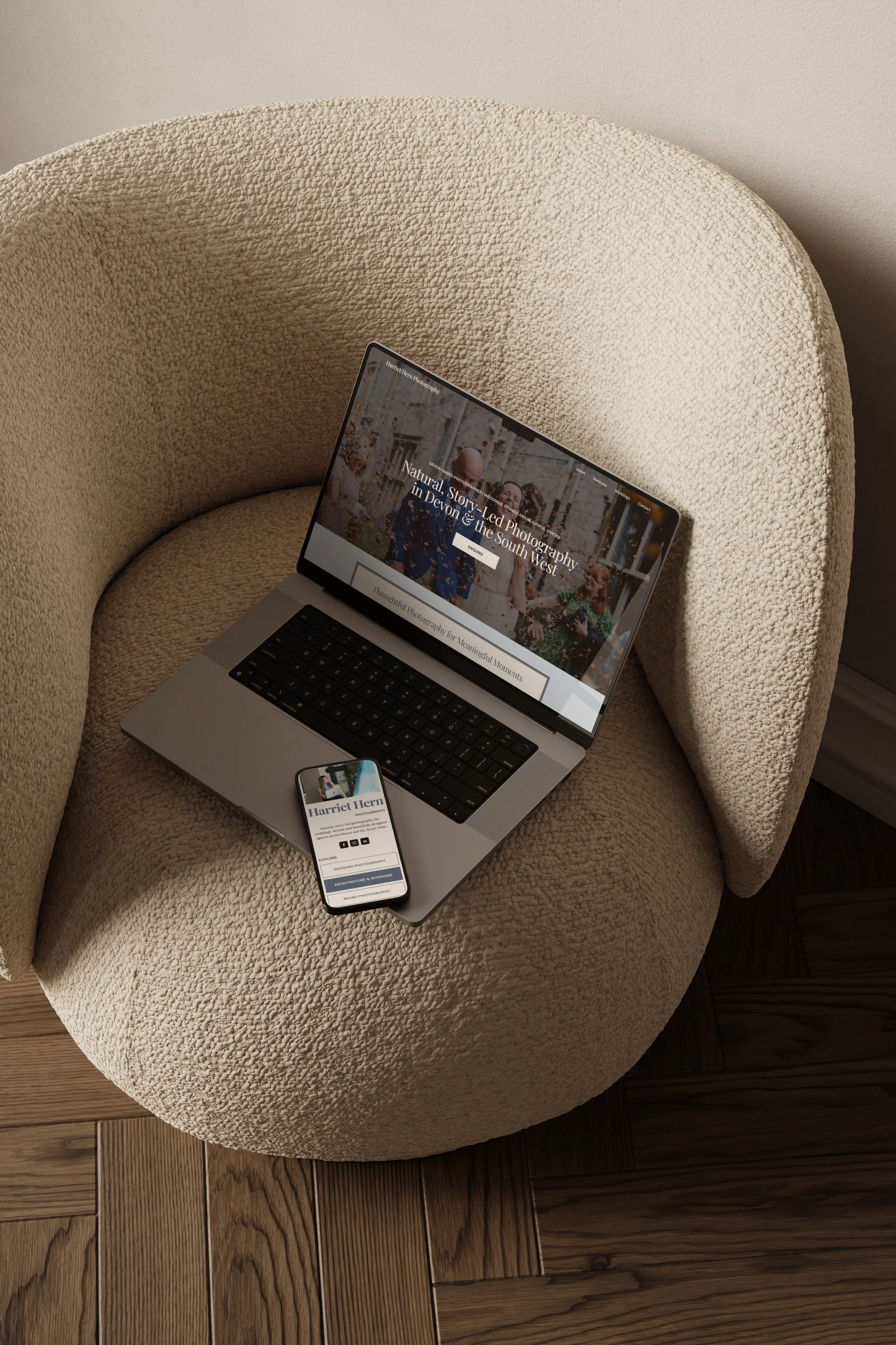 Open laptop and smartphone placed on a beige textured lounge chair on a wooden floor.