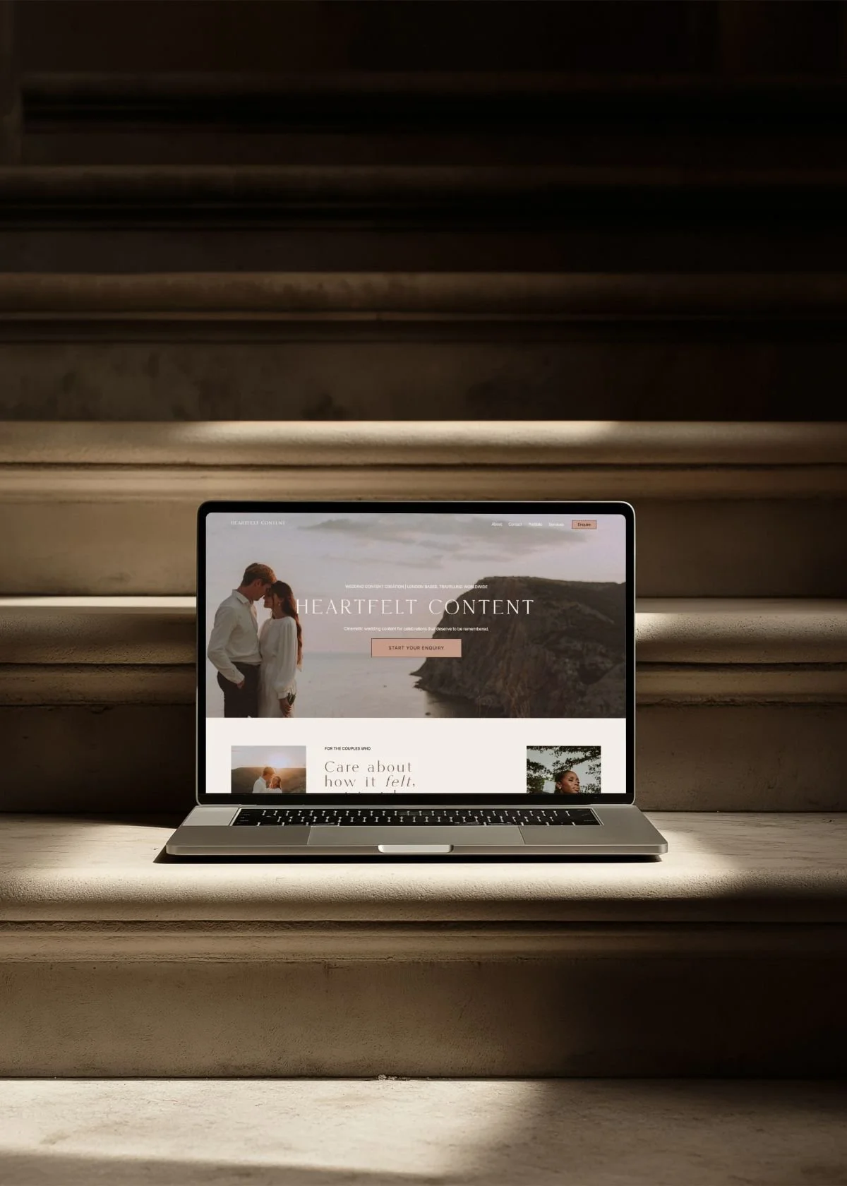 A laptop resting on stone steps in warm light, displaying the Heartfelt Content website homepage showing a couple embracing on a coastal clifftop, part of a website for content creator project by Studio Aretta