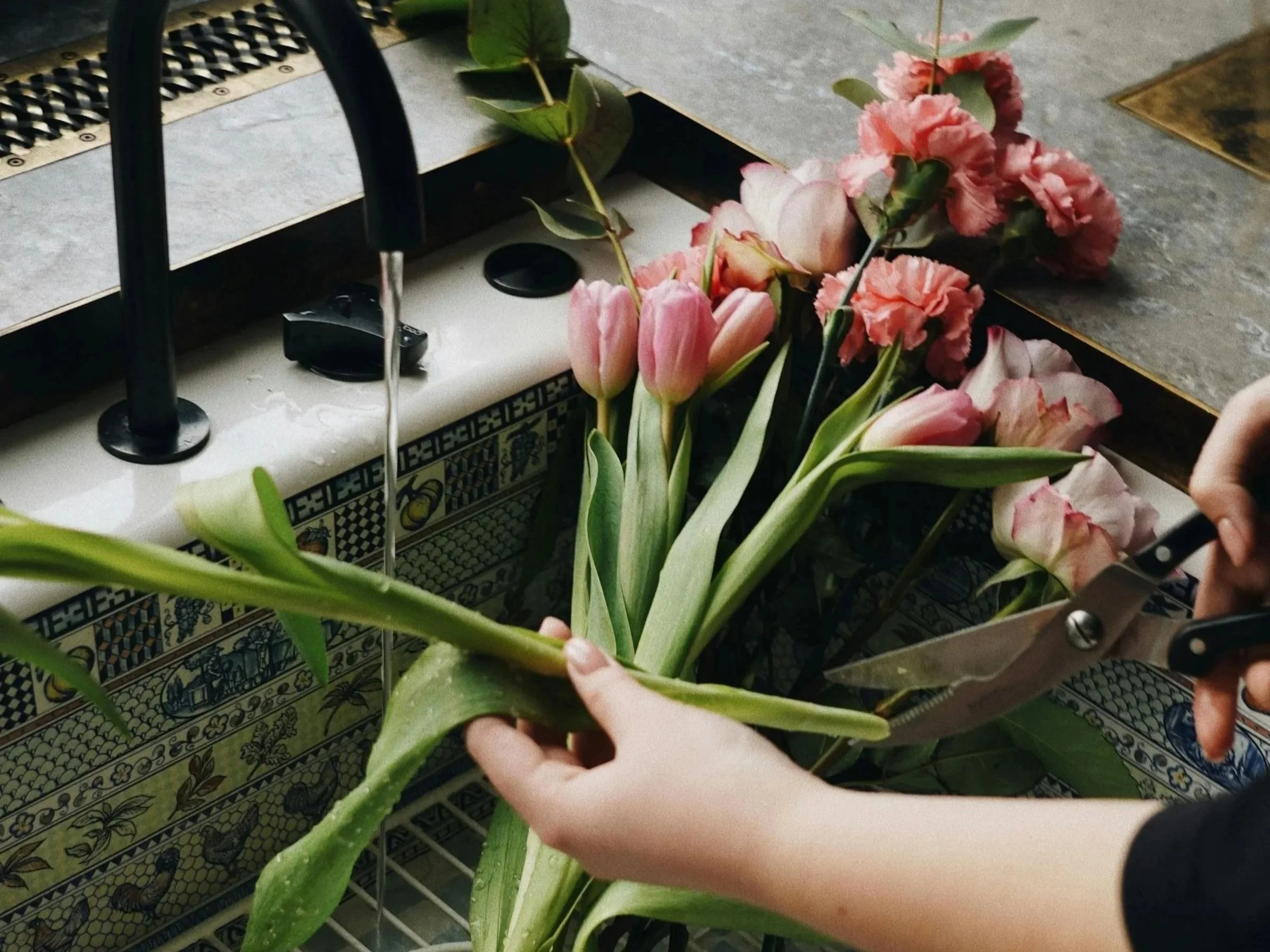 A selection of pink flowers in a tiled sink, being prepared for a vase, editorial image showcasing wedding pros on Studio Aretta blog.