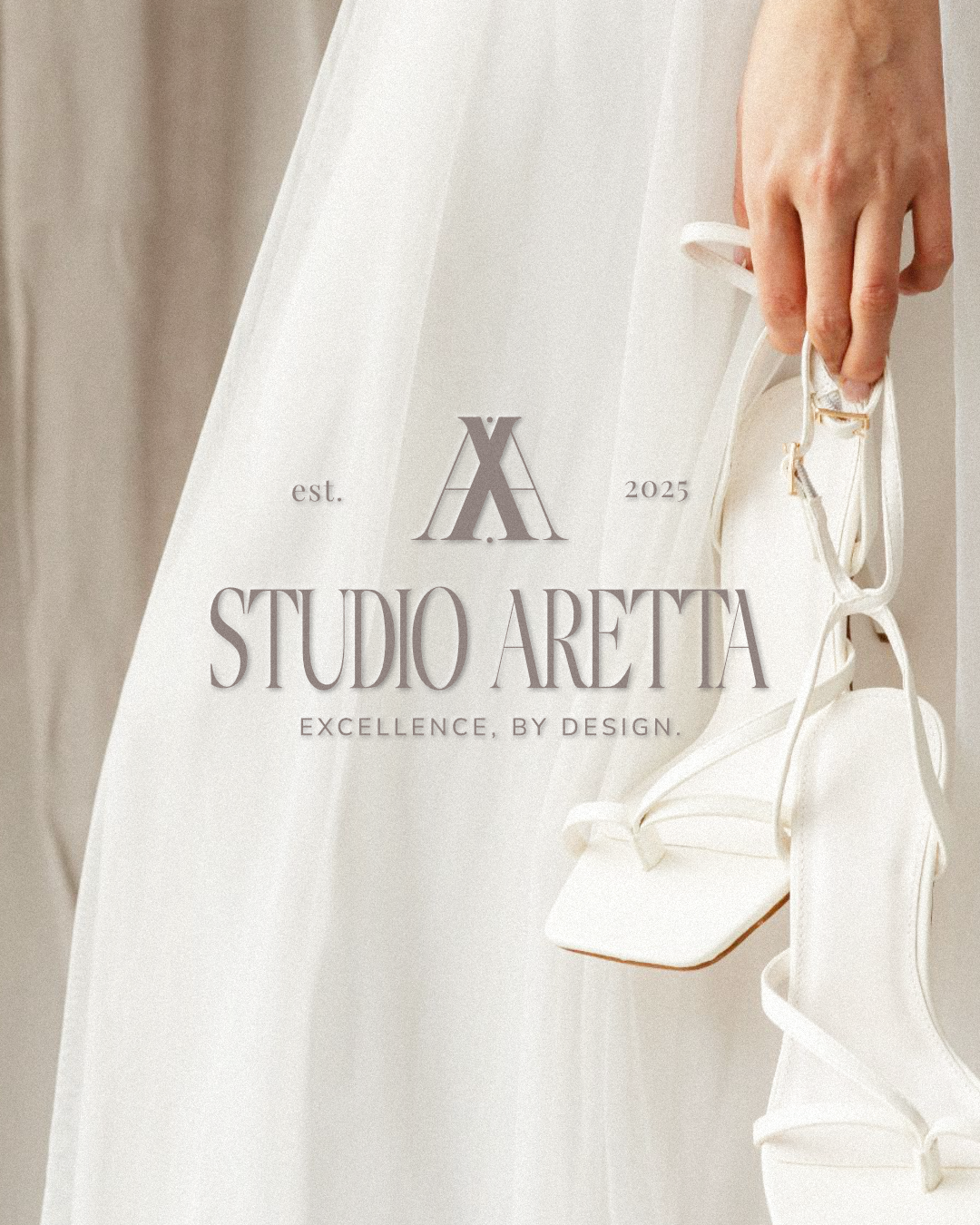 Close-up of a hand holding white high-heeled shoes, with text overlay for Studio Aretta, established 2025, featuring a stylish logo and slogan 'Excellence, by Design'.